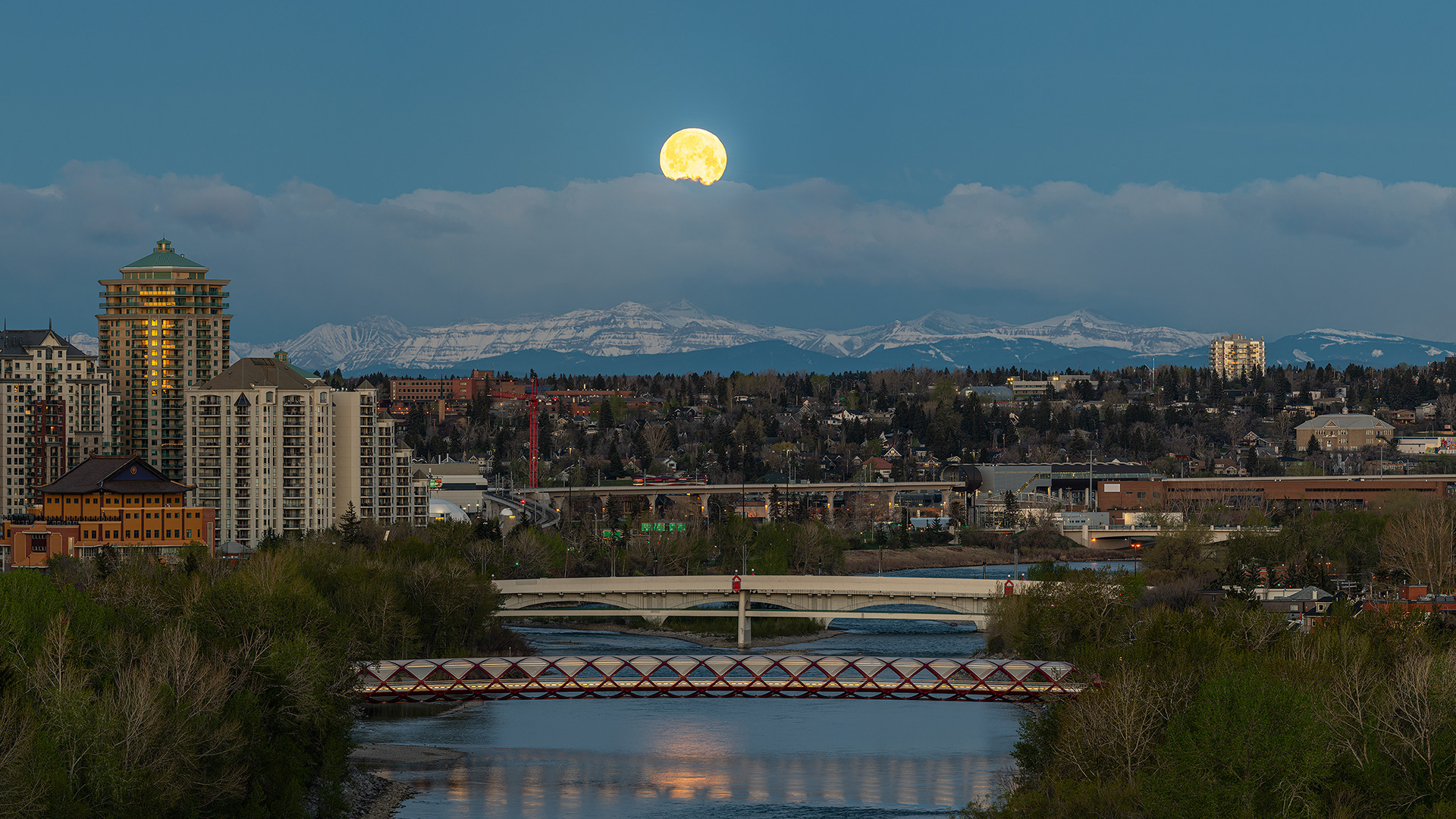 16x9 Panoramic Cityscape (5 shot) of the Bow River, Peace Bridge, and Moonset (Waning Gibbous phase @ 99.9%, elevation 2.5 degrees) (Civil Twilight/Golden Hour, Sun elevation -1.8 degrees), from the Crescent Heights Lookout Point, Calgary, AB