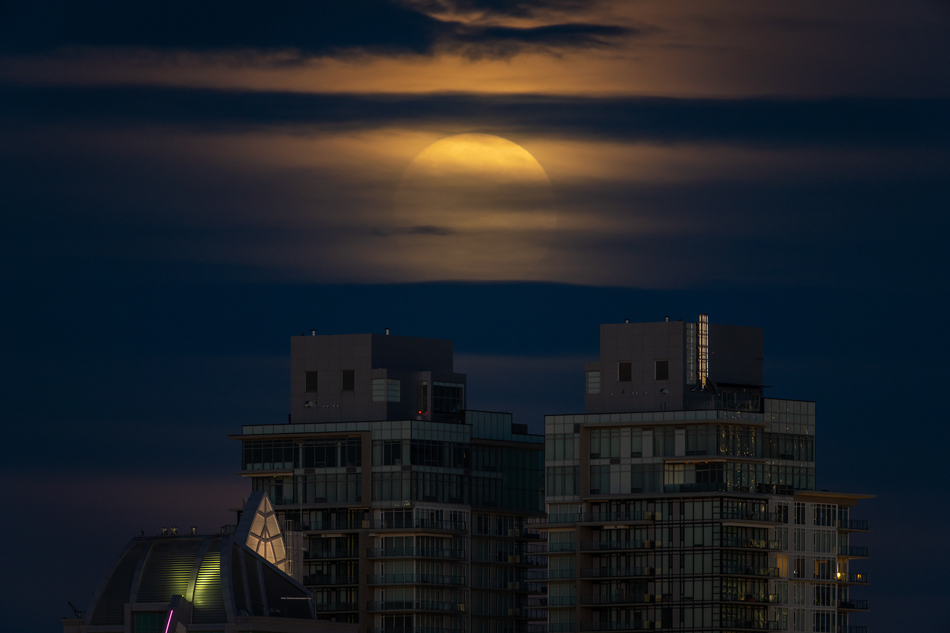 Moonset (Full phase @ 99.3%, elevation 3.9 degrees) (Nautical Twilight, Sun elevation -6.7 degrees) over twin tower downtown buildings, Tom Campbell's Hill Natural Park, Calgary, AB