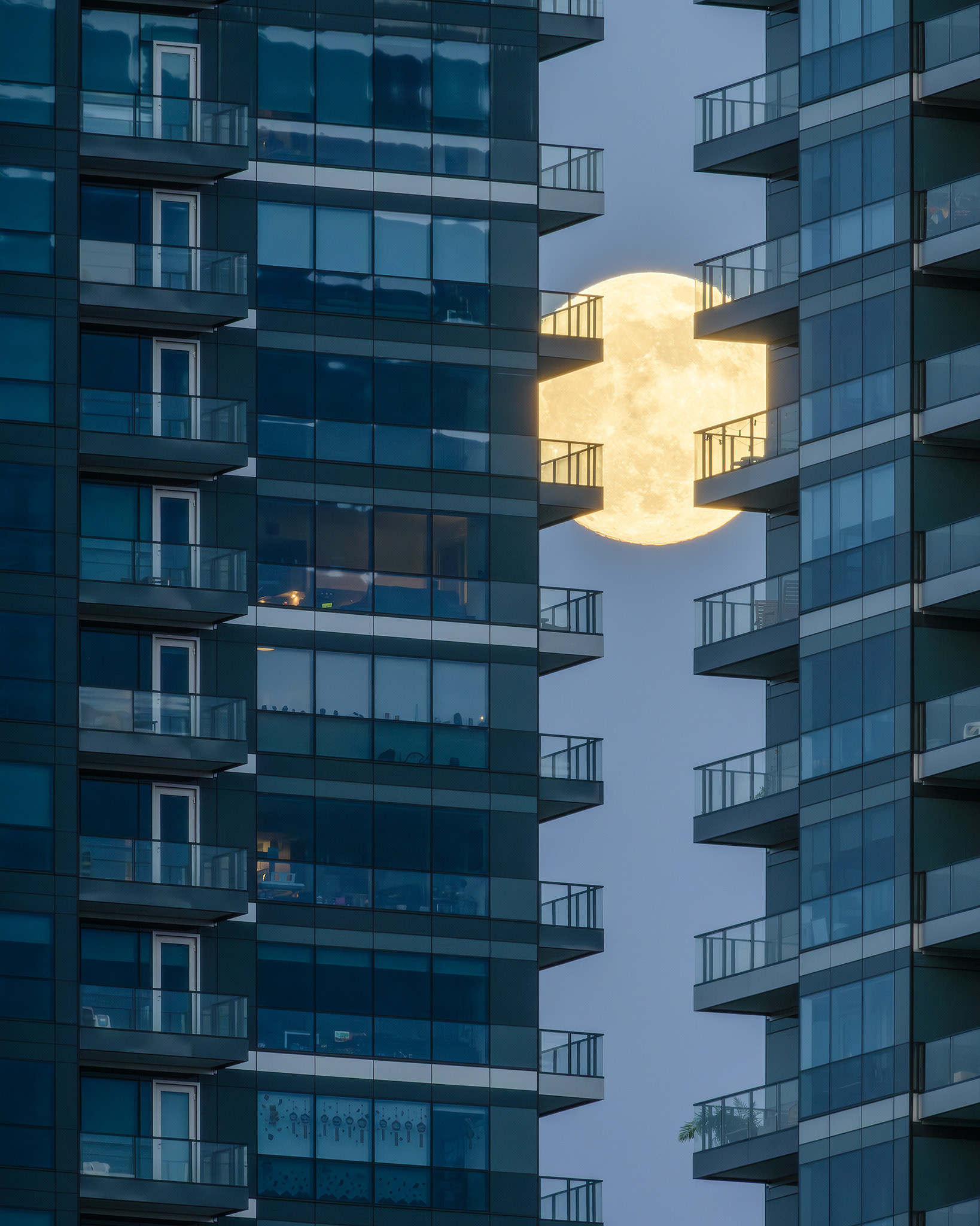 A photo of the Moon rising between a zoomed in portion of the West Village Towers during Civil Twilight, from Mewata (14 St SW) Bridge, Calgary, AB - April 22nd