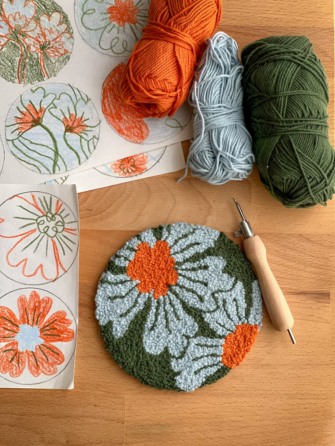 photo showing hand-made punch needle coaster, wool and sketches with floral patterns