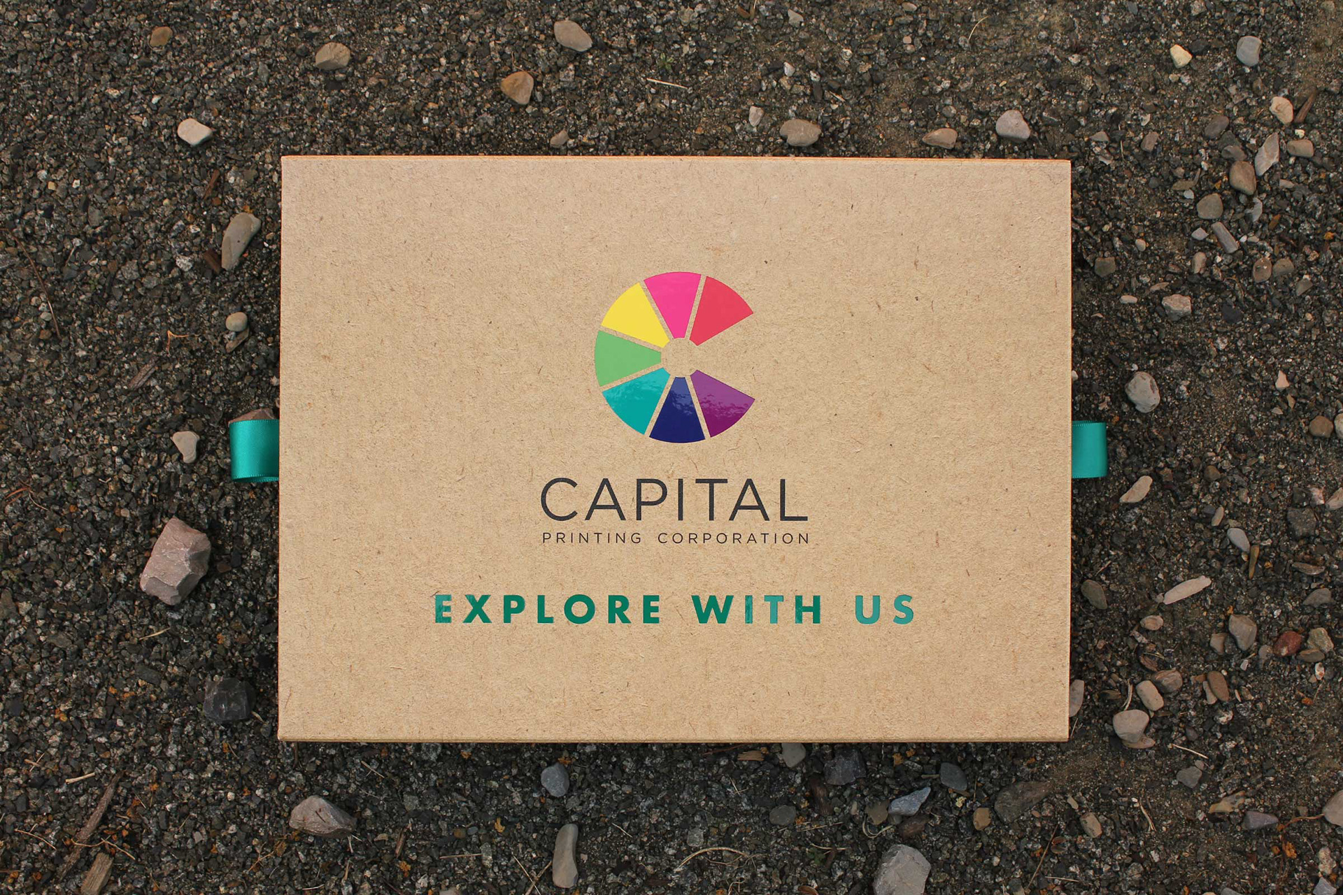 A marketing box for Capital Printing Corporation laying on the ground outside. The front reads "EXPLORE WITH US."