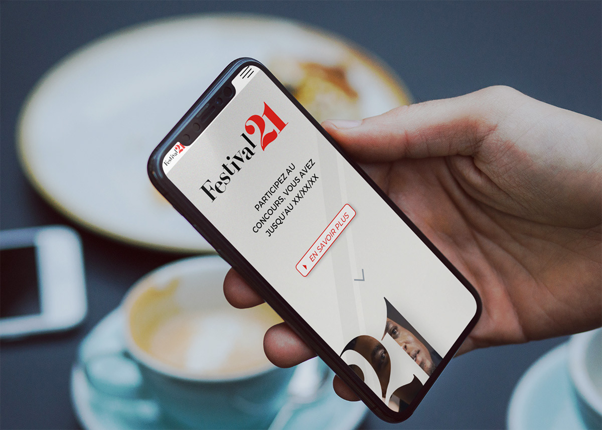 Une main tient un smartphone qui affiche la homepage du site sur mobile.