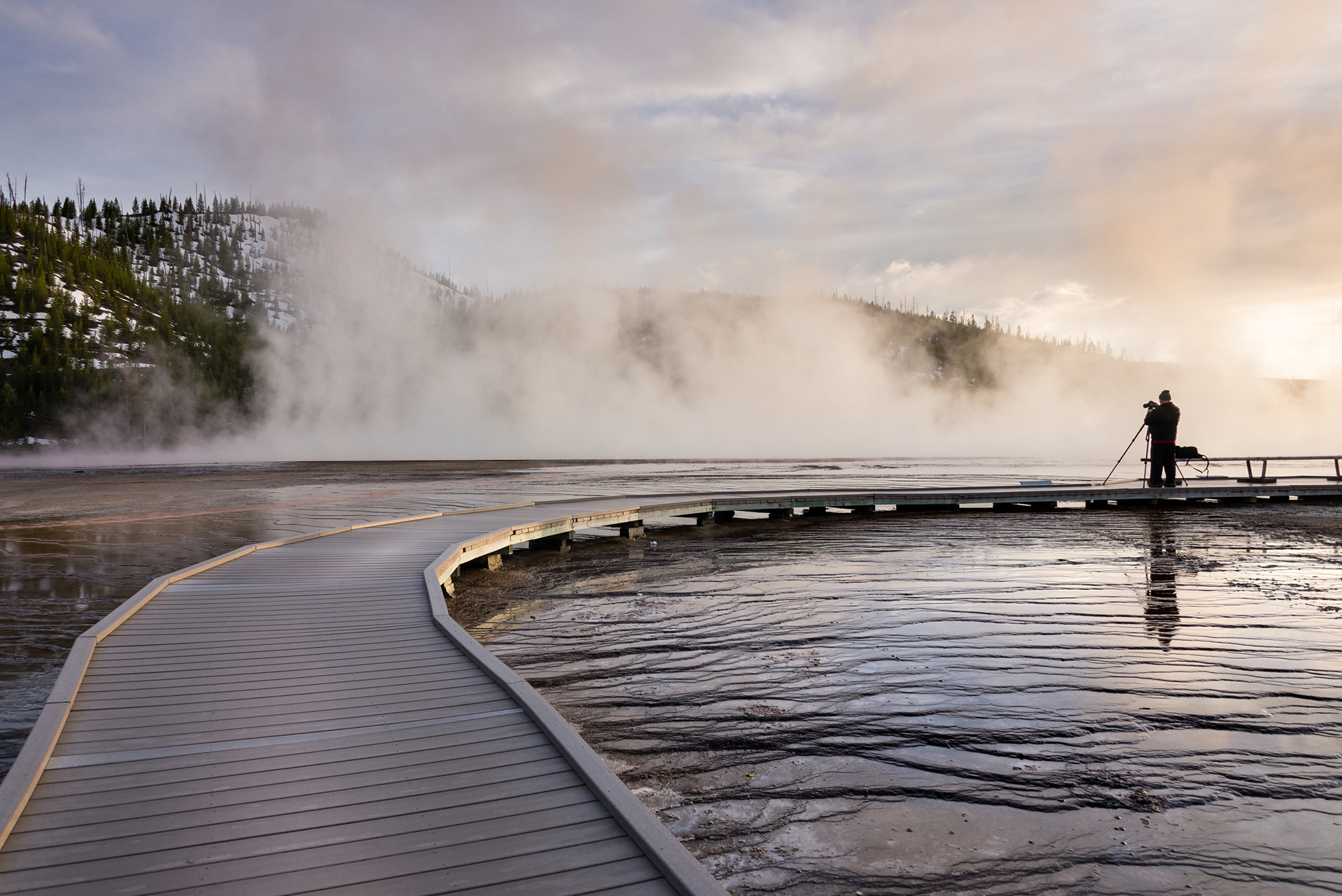 MAN IN THE NATURE - A man enjoying nature and his craft during a nice and cold sunset at Grand Prismatic Spring in Yellowstone National Park, Wyoming, USA.