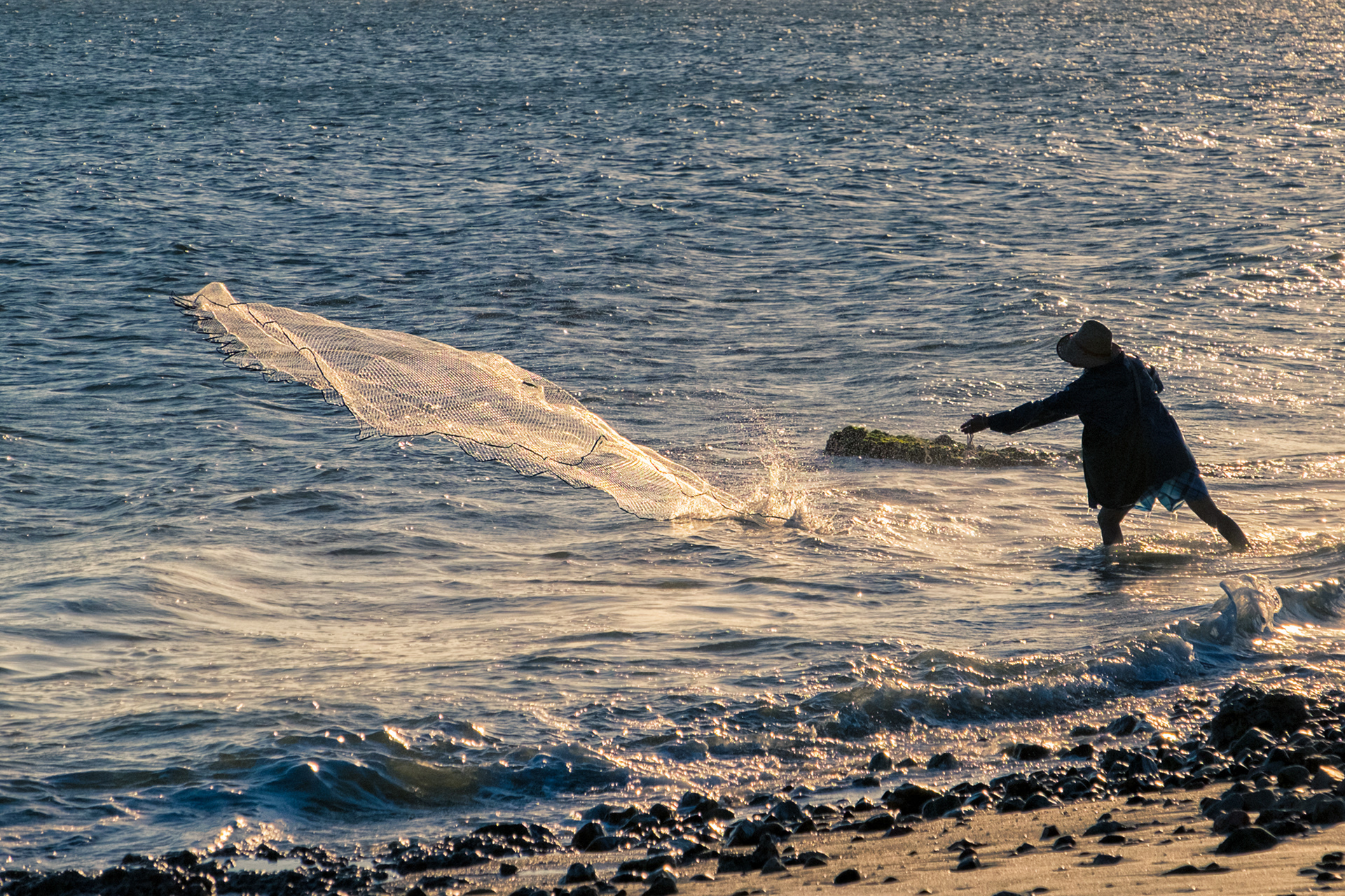 Fisherman in action - Local fisherman trying to catch some fish, on the shore of the beach, during the sunset at Las Flores, Maldonado, Uruguay.