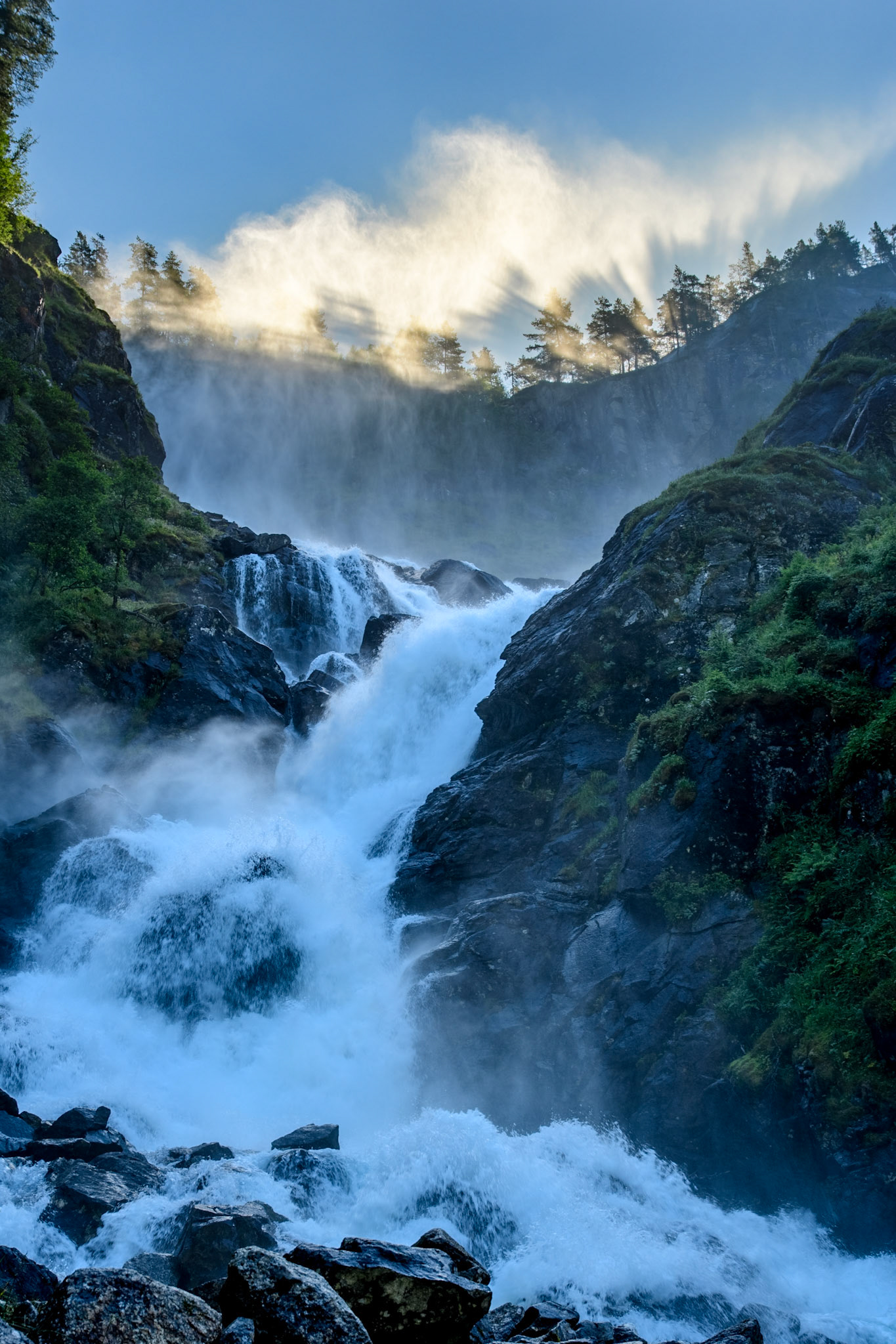 Latefossen waterval bij Odda in Noorwegen. De spray boven de waterval wordt mooi verlicht door de laagstaande zon die door de bomen schijnt. Latefossen waterfall near Odda in Norway. The spray above the falls is backlit by the sun shining through the trees on the ridge.