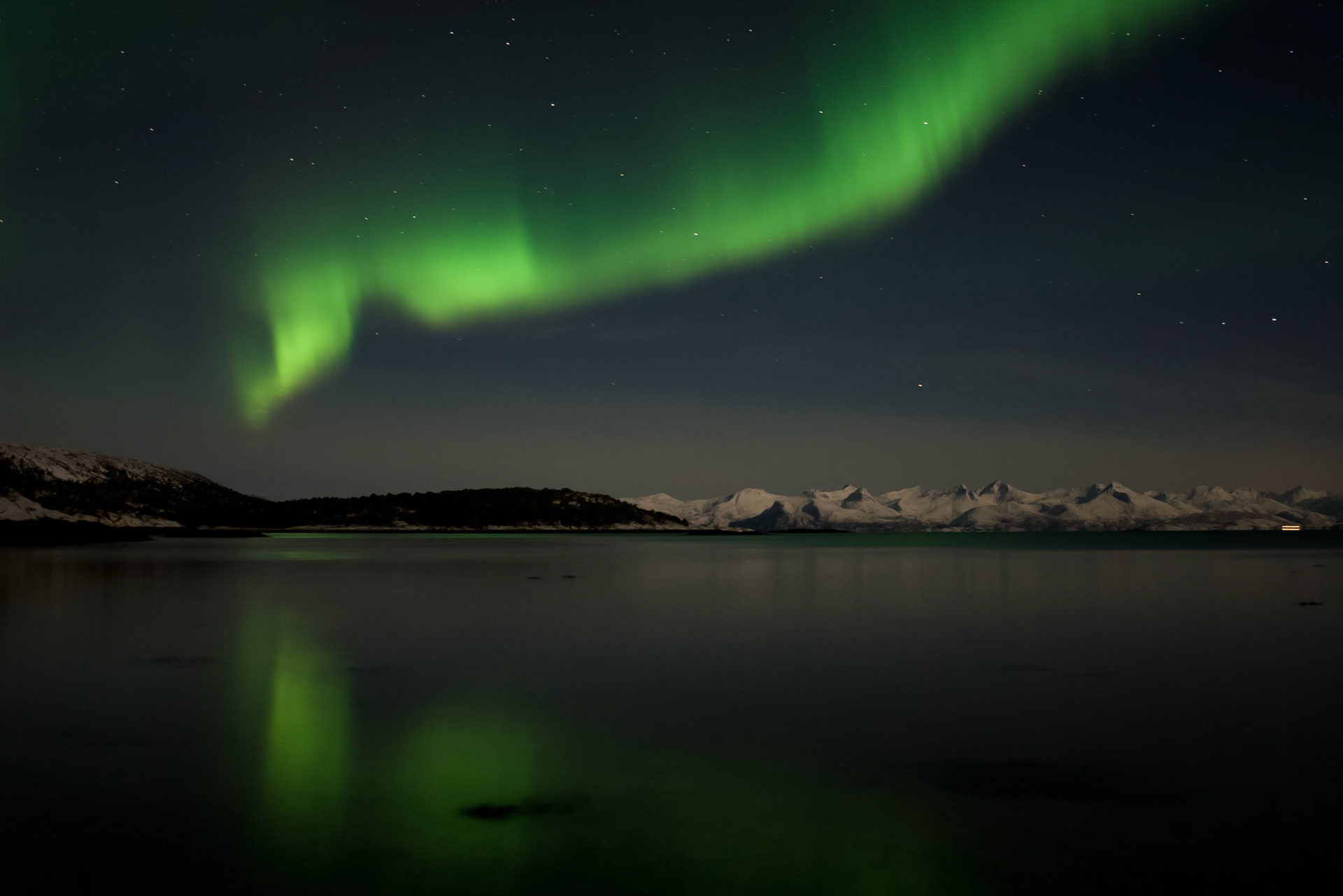Dansende lichtgordijnen boven de besneeuwde bergen, die worden beschenen door de volle maan.