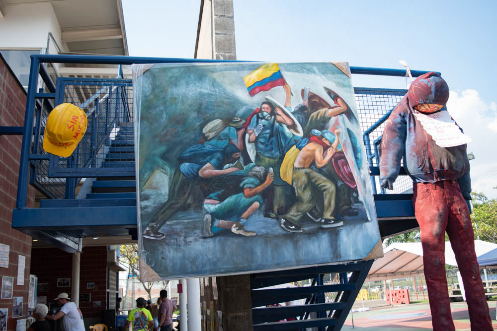 Instalación artística comunitaria en Siloé, Cali, con pintura mural y figura intervenida en espacio público, fotografía documental cultural.