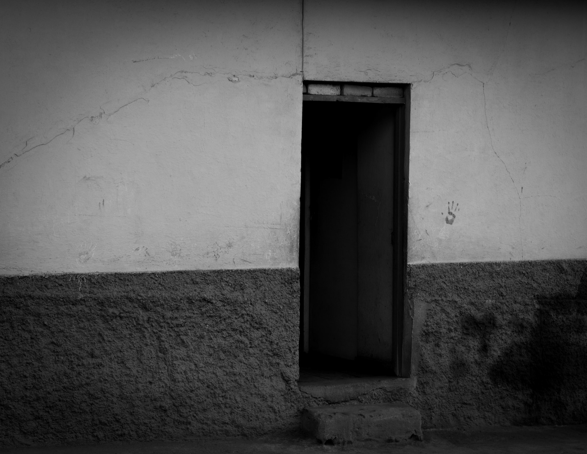 Fotografía en blanco y negro de puerta abierta en muro de vivienda rural con paredes agrietadas