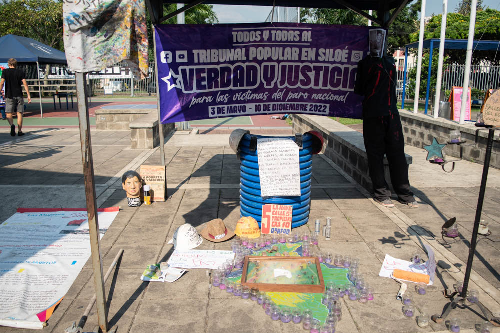 Instalación del Tribunal Popular en Siloé, Cali, con pancarta de verdad y justicia y ofrendas simbólicas en espacio público, fotografía documental social.