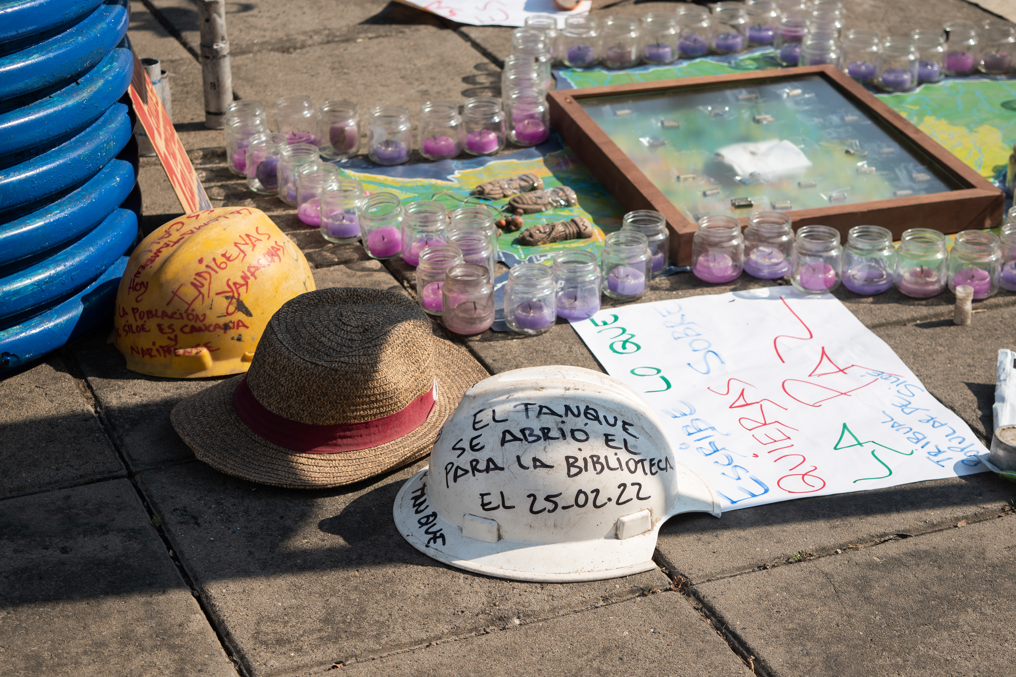 Objetos y ofrendas simbólicas del Tribunal Popular en Siloé, Cali, velas, cascos y carteles en instalación comunitaria, fotografía documental.
