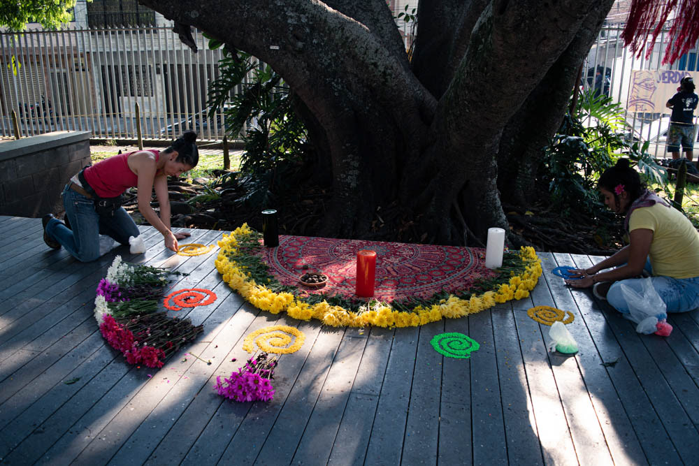 Ritual comunitario en espacio público de Siloé, Cali, con ofrenda floral y velas alrededor de árbol, fotografía documental social.