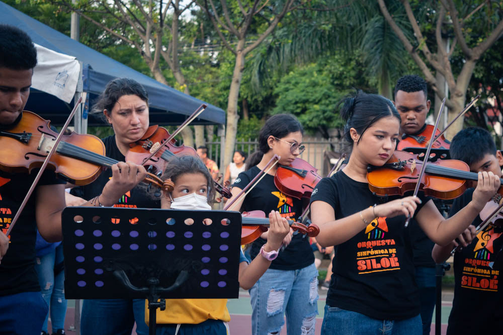 Orquesta juvenil tocando violines en Siloé, Cali, actividad cultural comunitaria en espacio público, fotografía documental.