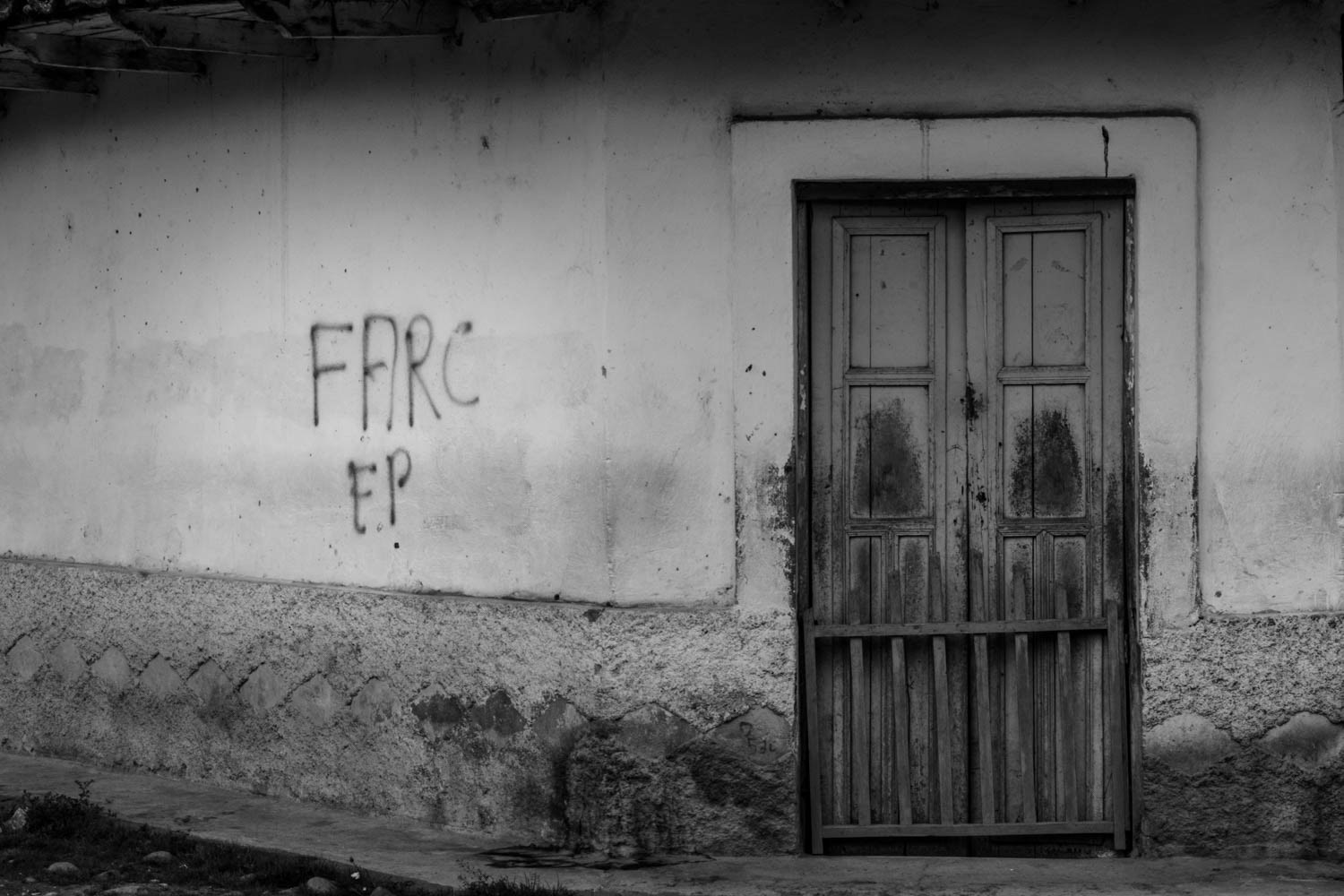 Fotografía en blanco y negro de puerta de madera cerrada en vivienda rural con grafiti en pared desgastada