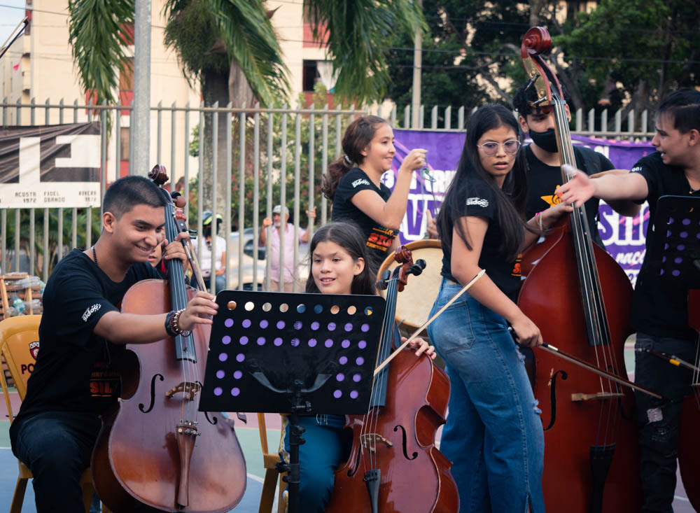 Orquesta juvenil tocando violonchelos en espacio público de Siloé, Cali, fotografía documental de actividad cultural comunitaria.