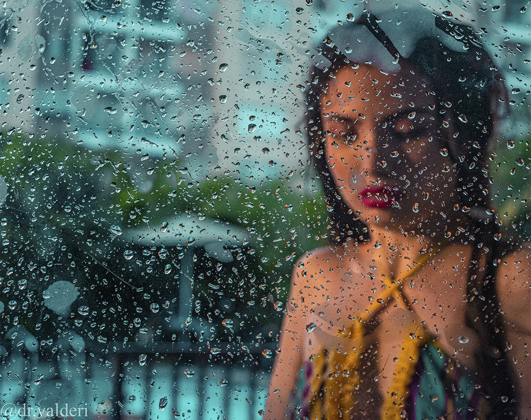 Mujer tras vidrio con gotas de lluvia, fotografía artística.