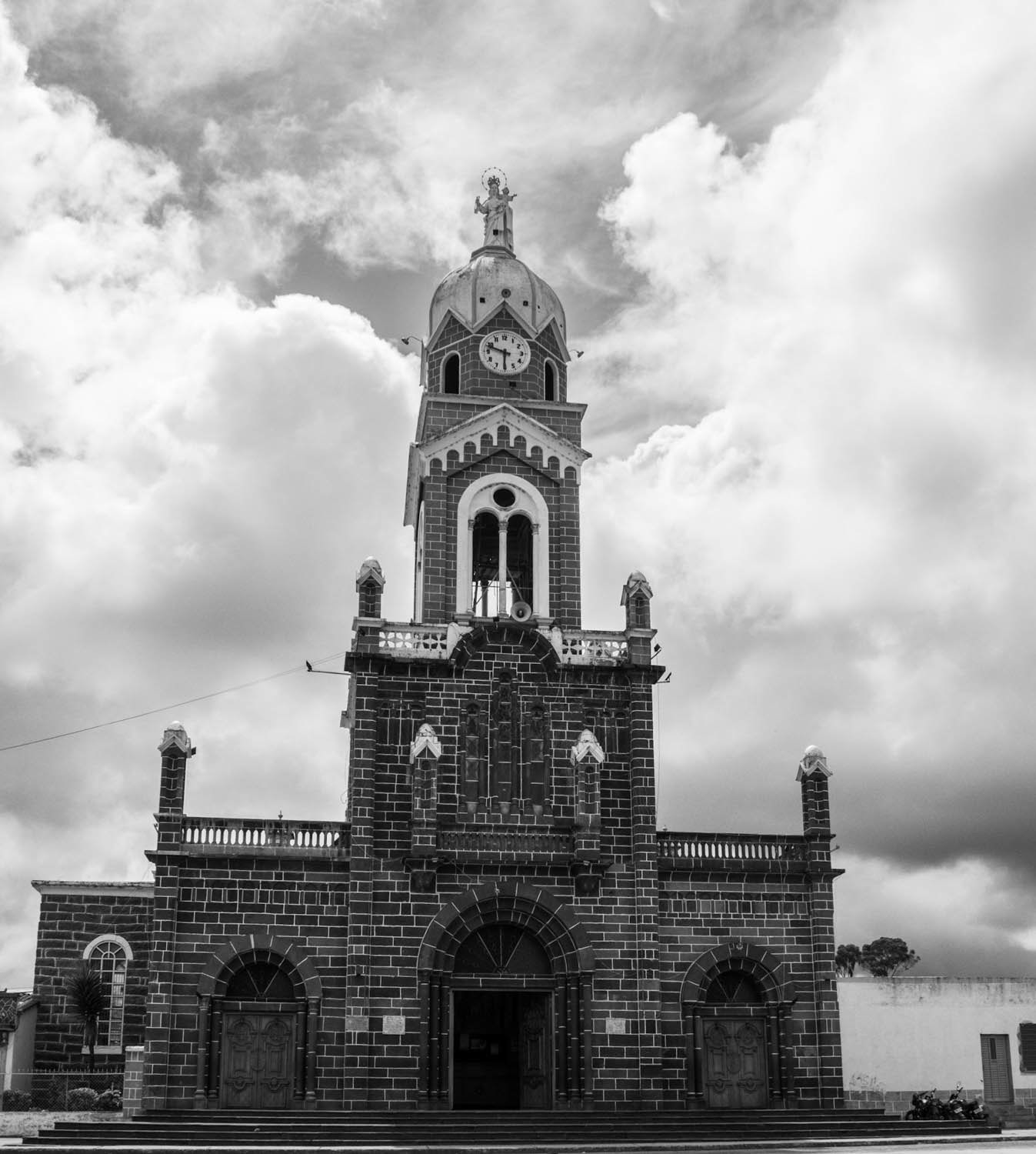 Fotografía en blanco y negro de torre de iglesia con reloj y cúpula, arquitectura religiosa destacada sobre cielo nublado