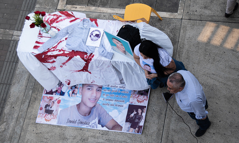 Instalación memorial en espacio público de Siloé, Cali, con fotografías de víctima y ofrenda simbólica, fotografía documental social.