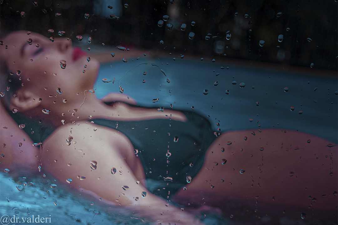 Mujer flotando en piscina vista a través de gotas de agua, fotografía artística.