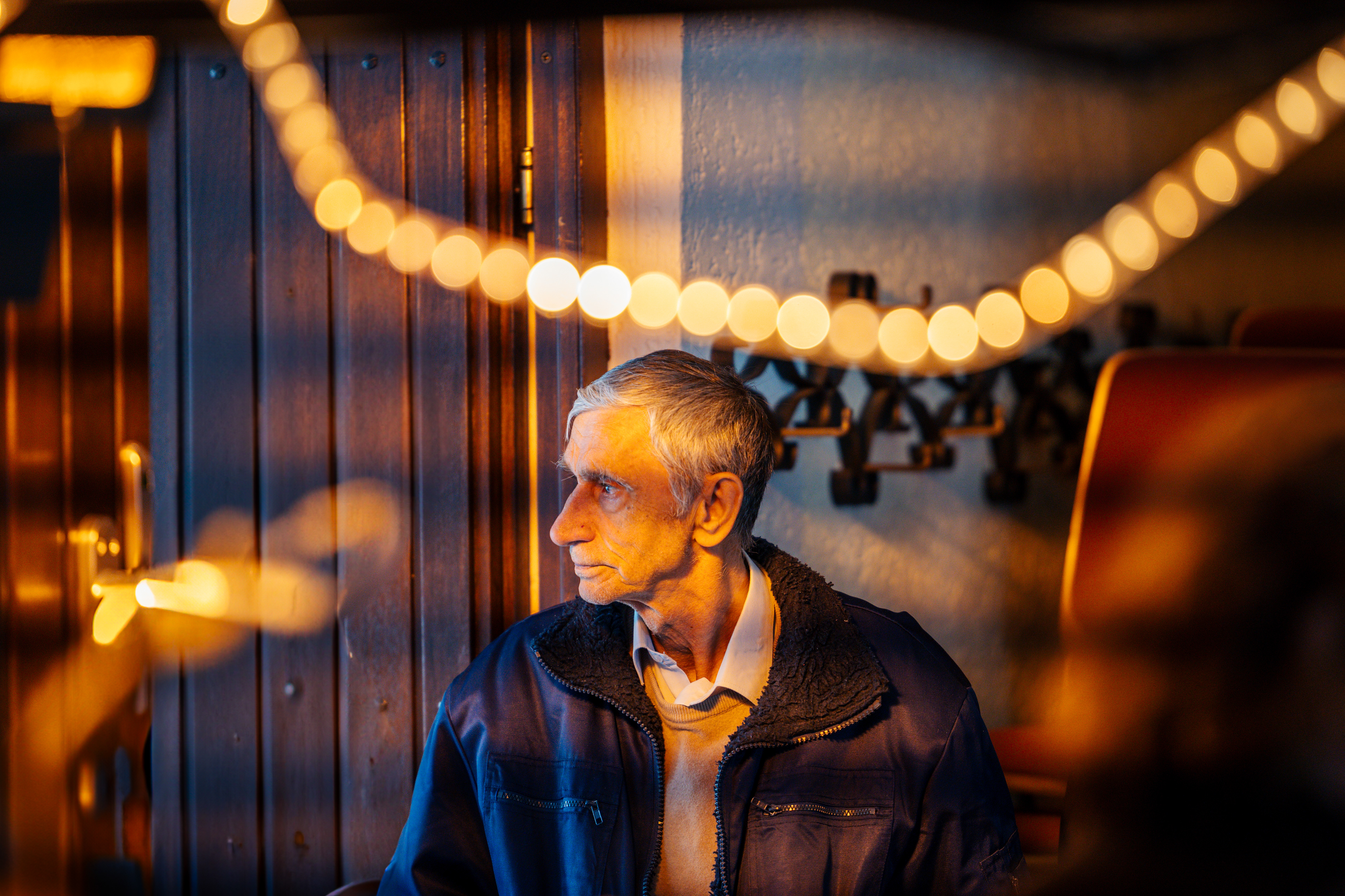 Älterer Mann, der nachdenklich zur Seite schaut und dabei von einer warmweißen Lichterkette beleuchtet wird