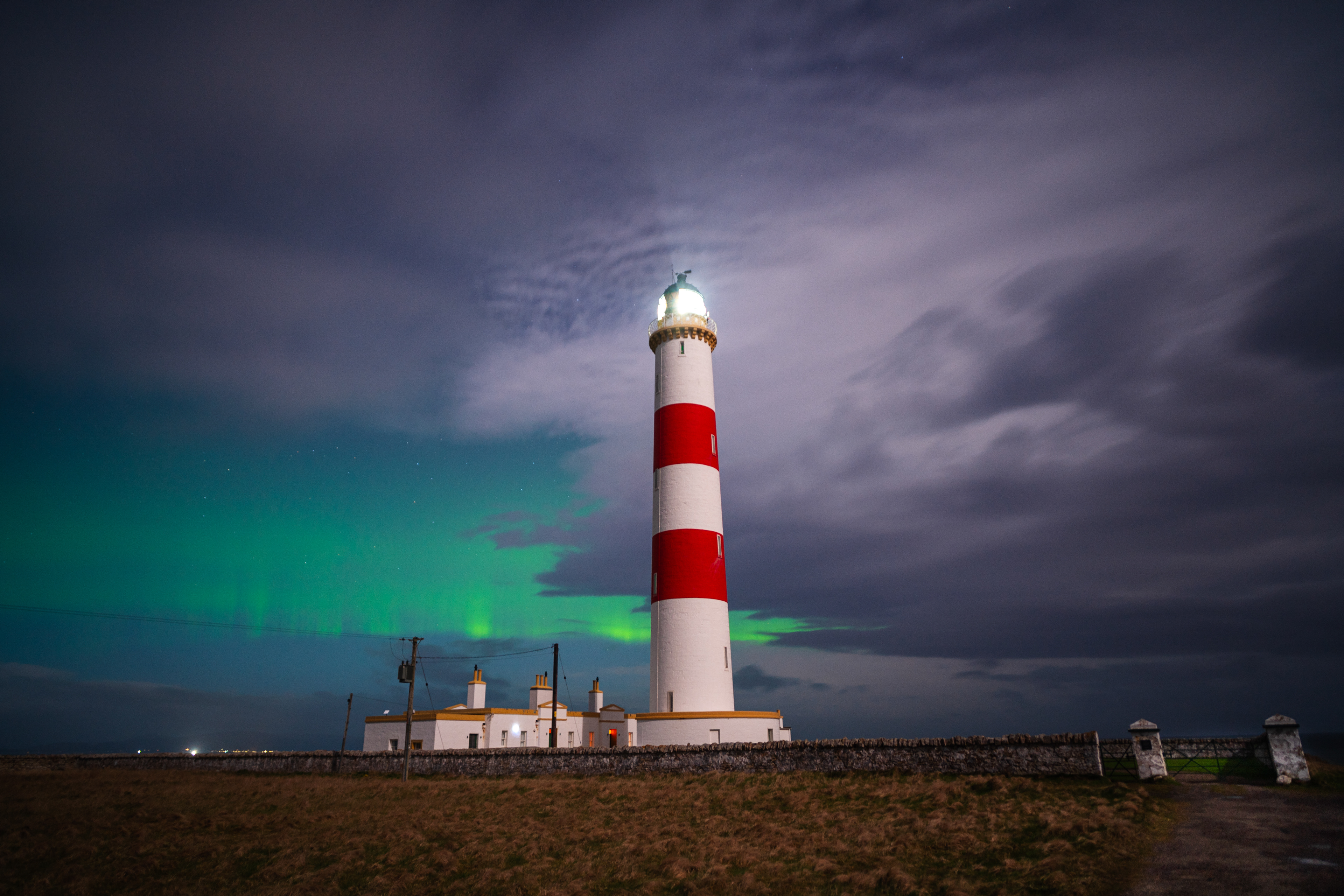 rot-weißer Leuchtturm mit Wolken und Aurora im Hintergrund