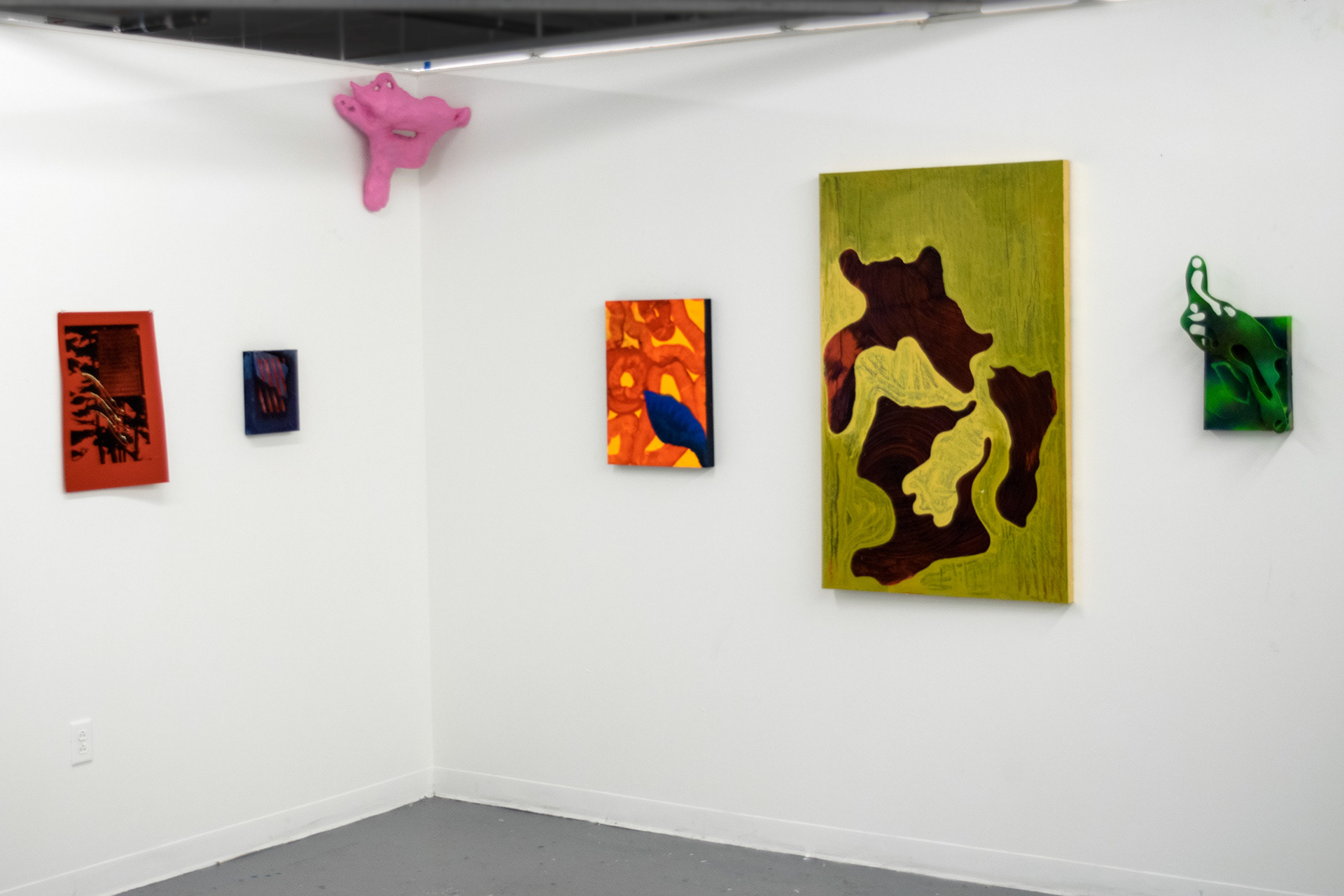 This photograph documents other aspects of an art installation which includes several types of objects: paintings, prints, drawings, and a paper mache sculpture affixed to the wall.