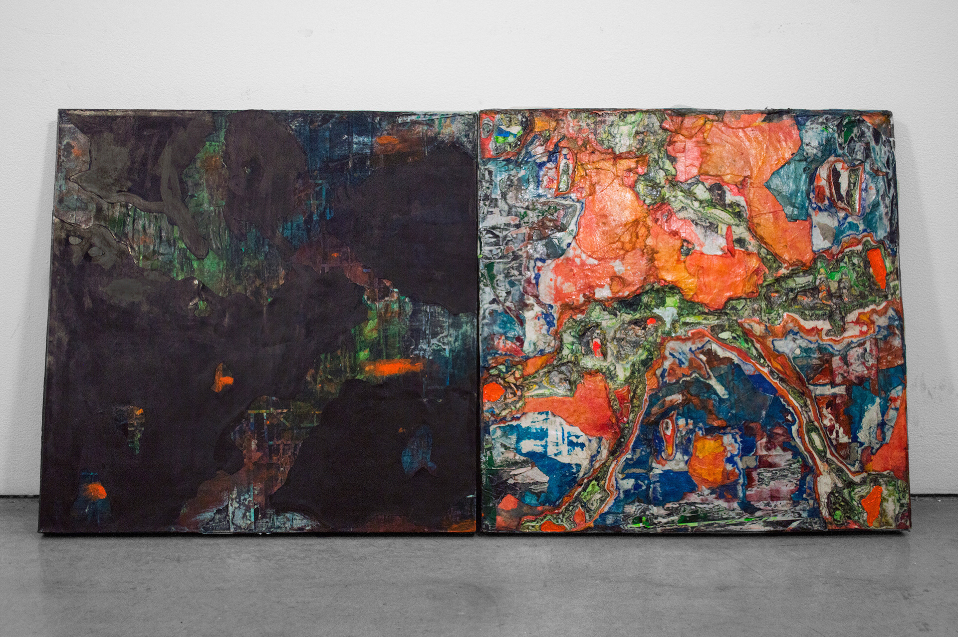 This photograph documents an abstract diptych. There are two square panels leaning against the wall, which bear abstract marks made of many layers cut and sanded paper and paint.