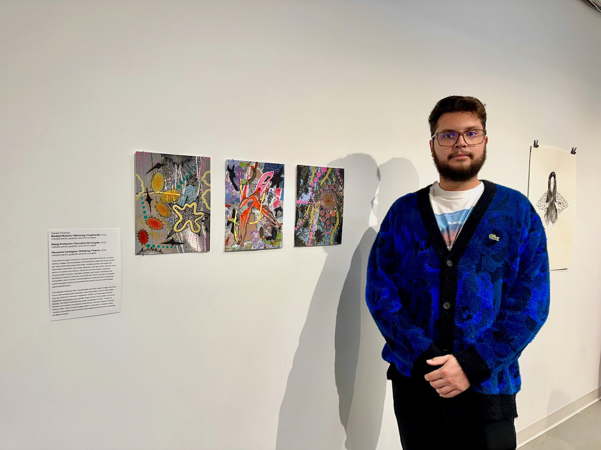 Artist Daniel Thomas standing beside his collage-drawings in an art gallery October 2025