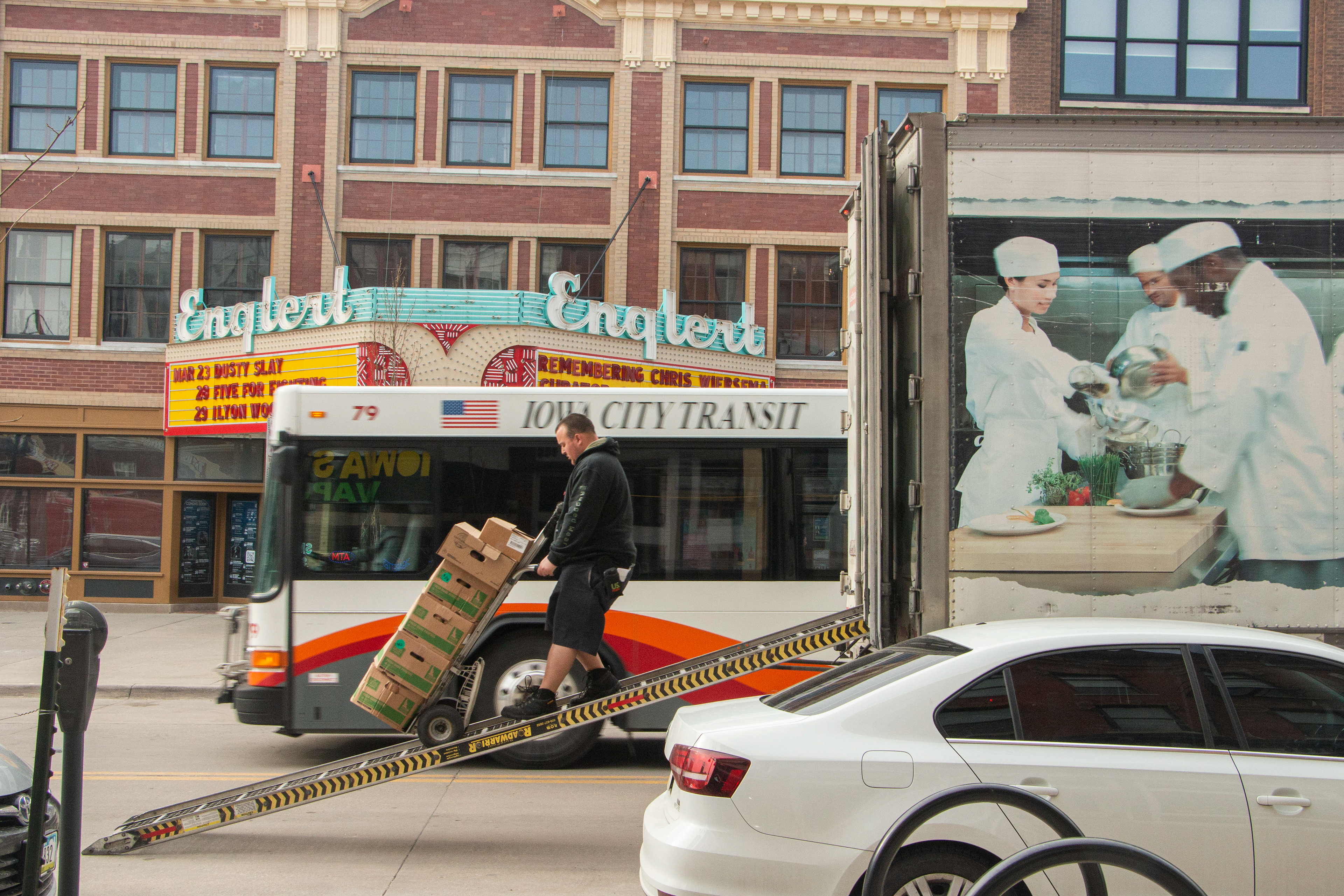 A truck driver unloads the products while the city bus passes on the back, typical downtown morning routine on March 24, 2024, Iowa City, IA.