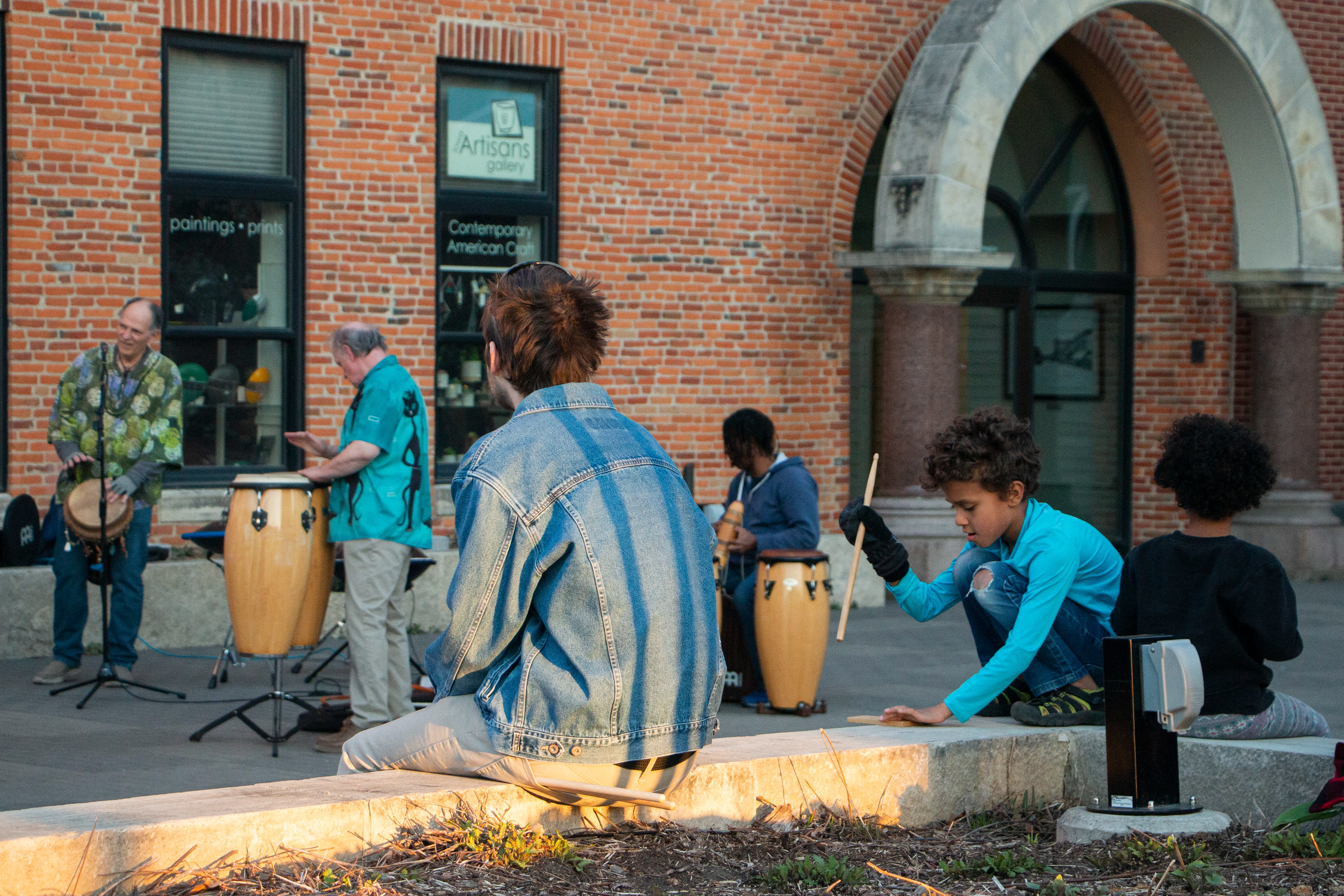 Hippie senior band plays while pedestrians watch and one of the member's kid plays with the drum stick on April 9, 2024 in Downtown Iowa City, IA