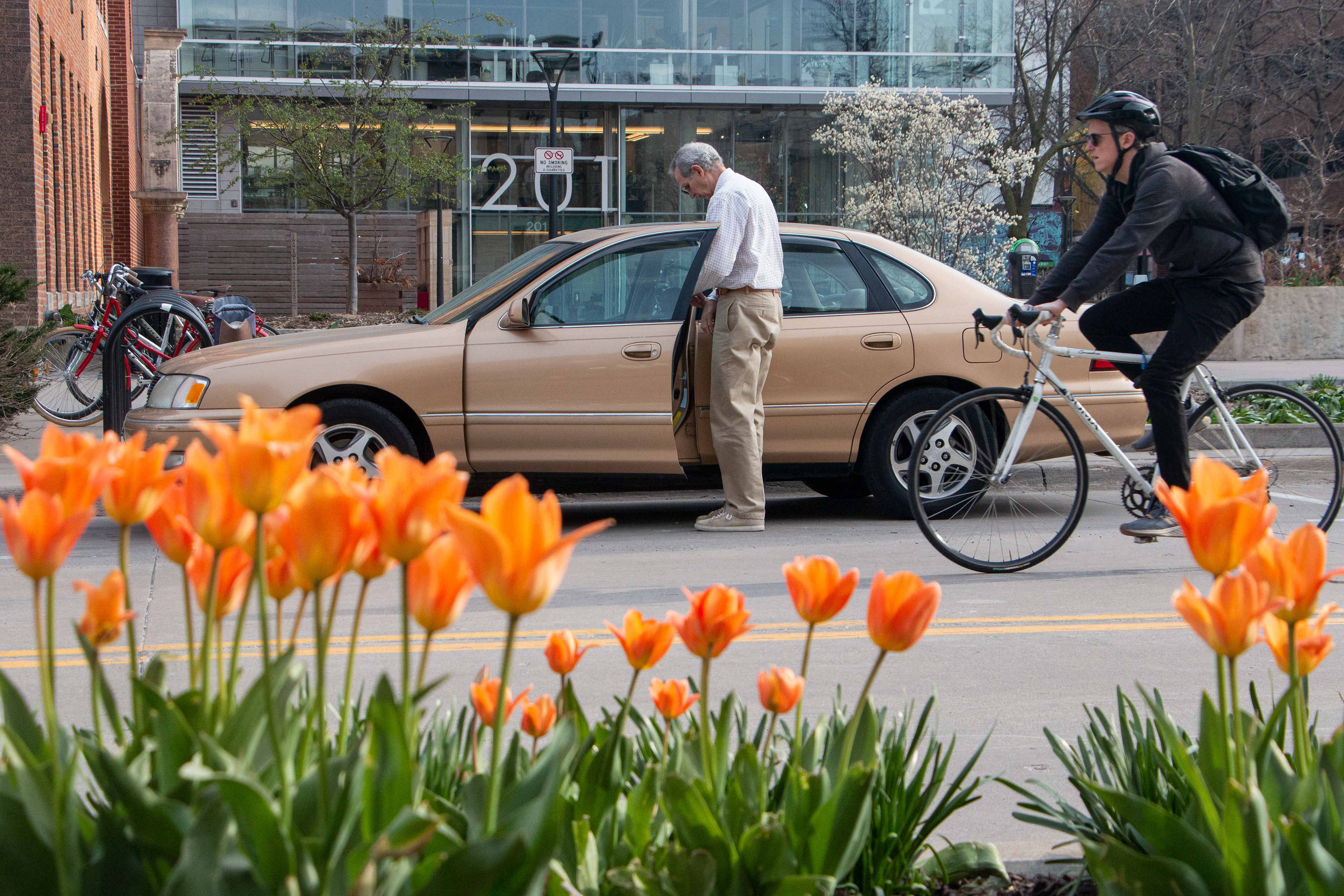 Old men gets out of his car while a biker passes by during early spring on April 2, 2024 in Downtown Iowa City, IA