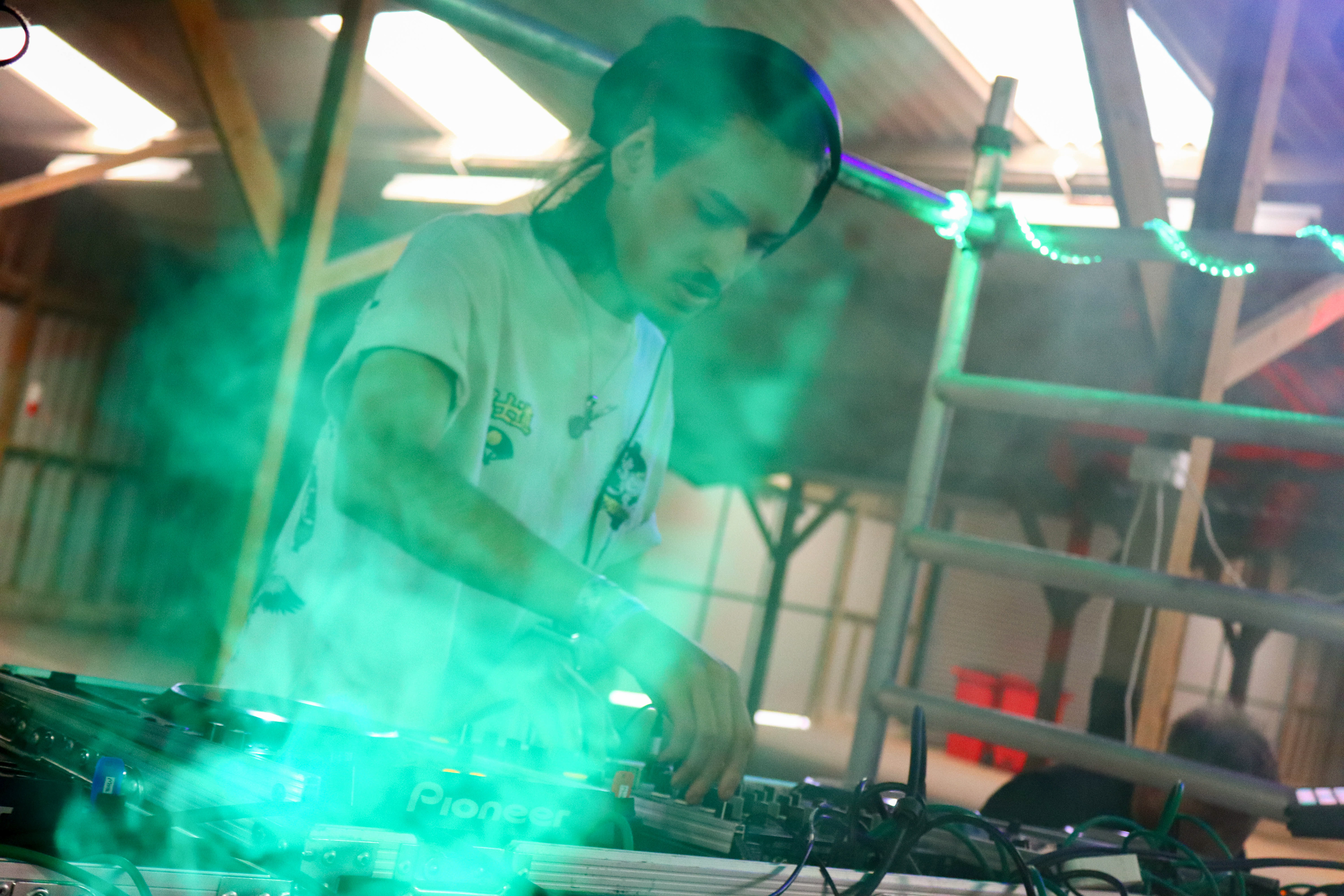 This is an image of Moose DJing at Shayde Fest 2023, there's a slight glow in front of him from a fog machine and a green light.