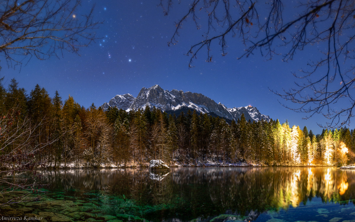 Bright stars of Orion constellation shine in a moonlit night over Lake Badersee, Bavaria.