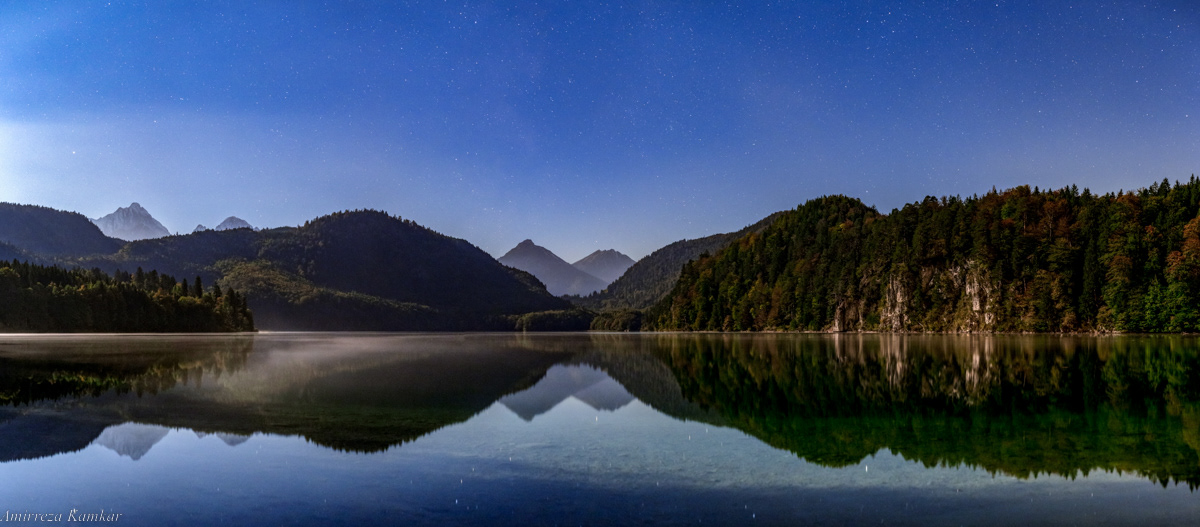 Panoramic view of a moonlit night in Lake Alpsee, Bavaria, Germany.