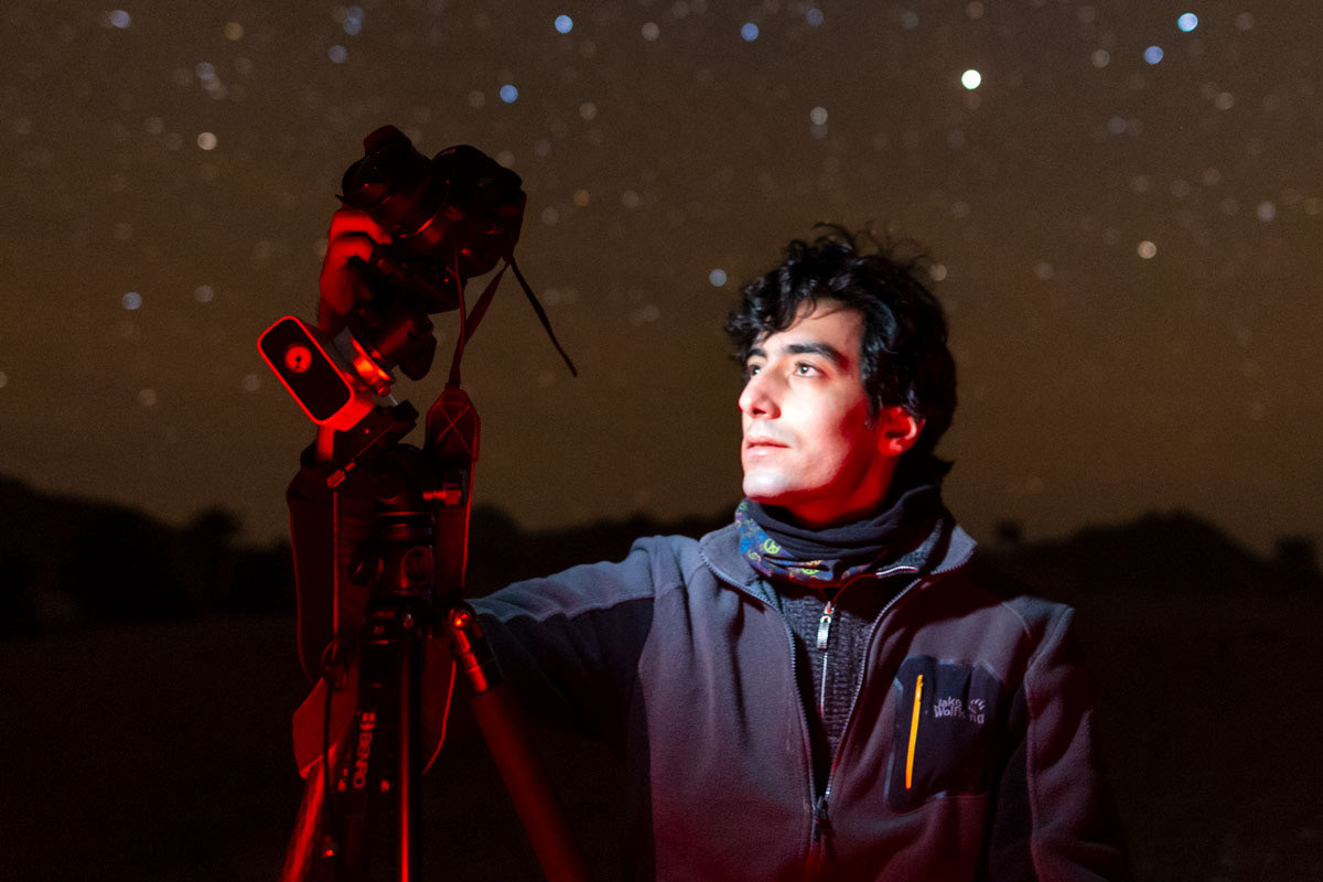 A photographer at night, with camera and tripod and stars in the background.