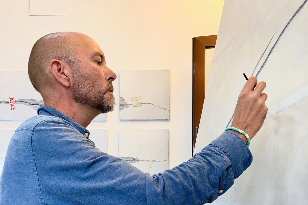 Kursleiter Egmont Hartwig malt konzentriert an einer grossen Leinwand in seinem Atelier in Dornbirn, im Hintergrund mehrere minimalistische Wandbilder.
