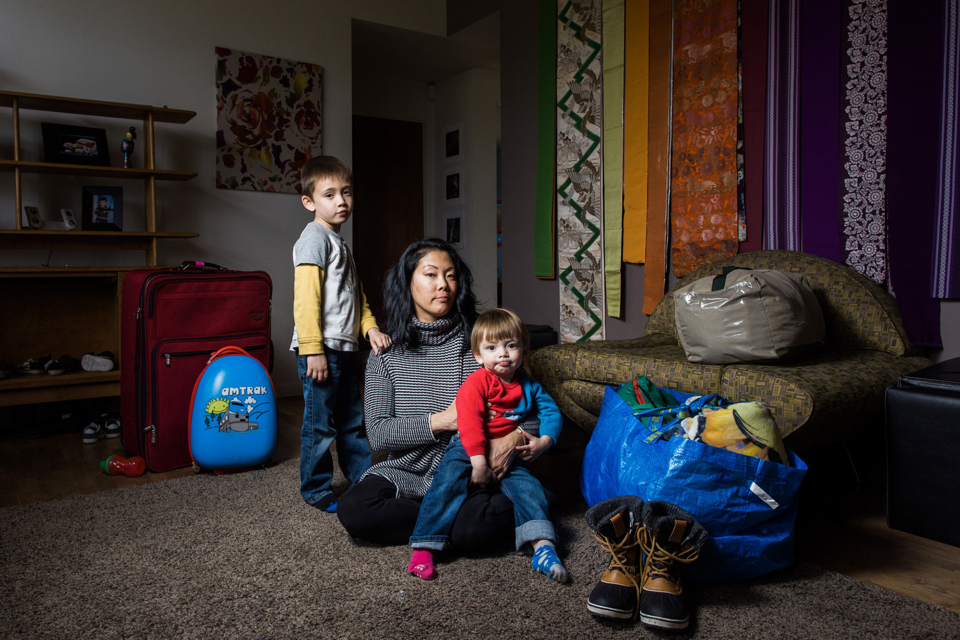 Seattle, WA—Mari Hirabayashi, 42, sits in her living room with her children, Theodore, 5, and Ely, 1, Kennedy. Photo by Kayla Isomura, as created for The Suitcase Project