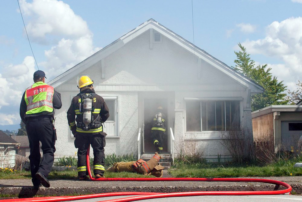 New Westminster, B.C.—A firefighter candidate enters an empty house in the Sapperton area of New Westminster as part of the city’s firefighter and rescue training scenarios. Candidates removed props from the house, cleared smoked and hosed the house from the outside and inside. The house, soon to be demolished, was granted use from the city. Photo by Kayla Isomura