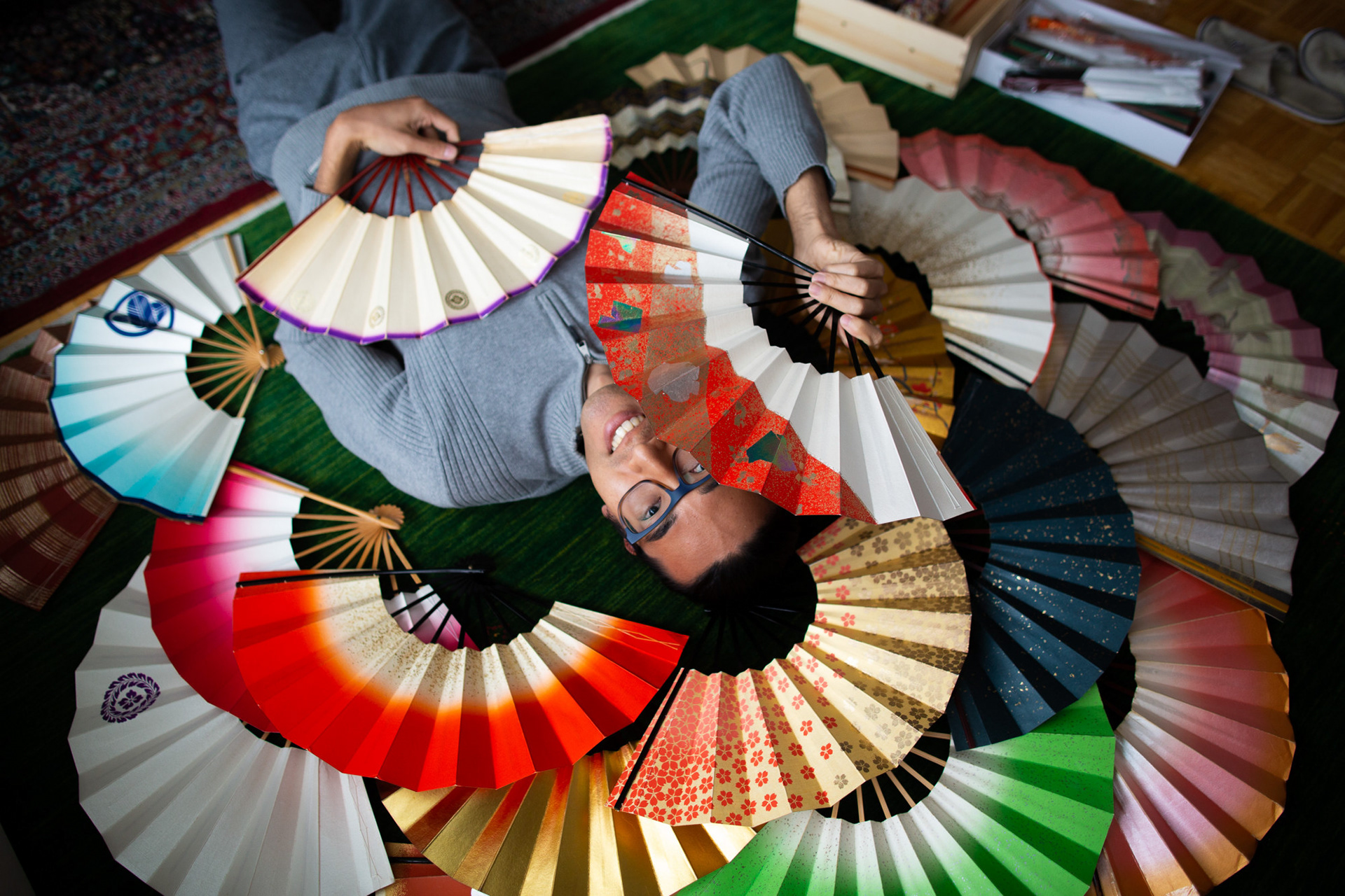 Ottawa, Ont.—Hugo N. lays on the floor of his apartment, surrounded by his collection of Japanese fans. His interest in the fans stems from his relationship to his Japanese heritage. As a teenager, he participated in Japanese traditional dance classes and was gifted his first two fans from a dance teacher in São Paulo, Brazil. While he has never counted his collection, N. estimates to have at least 100 fans. Photo by Kayla Isomura, as shot for The Pioneer