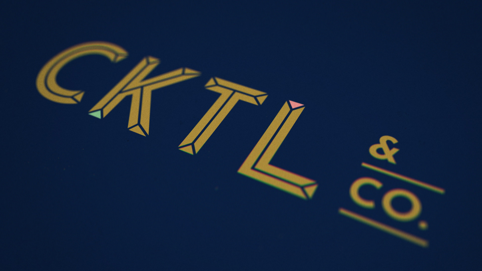A close-up macro view of the logo for Cocktail and Co., with gold text on a dark blue background.
