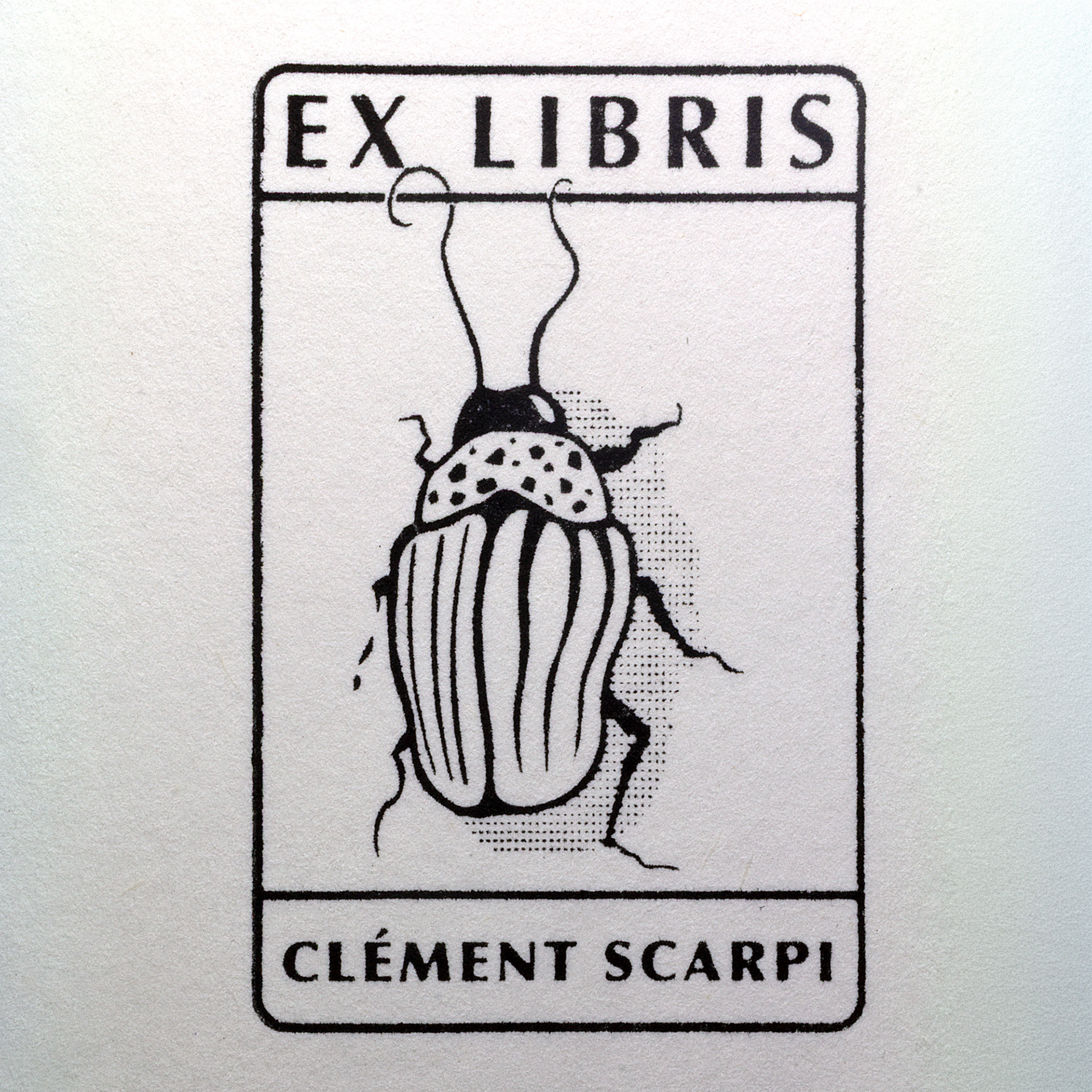 A rubber stamp with a insect illustration and the text “EX LIBRIS CLÉMENT SCARPI” lies next to its stamped impression on white paper.