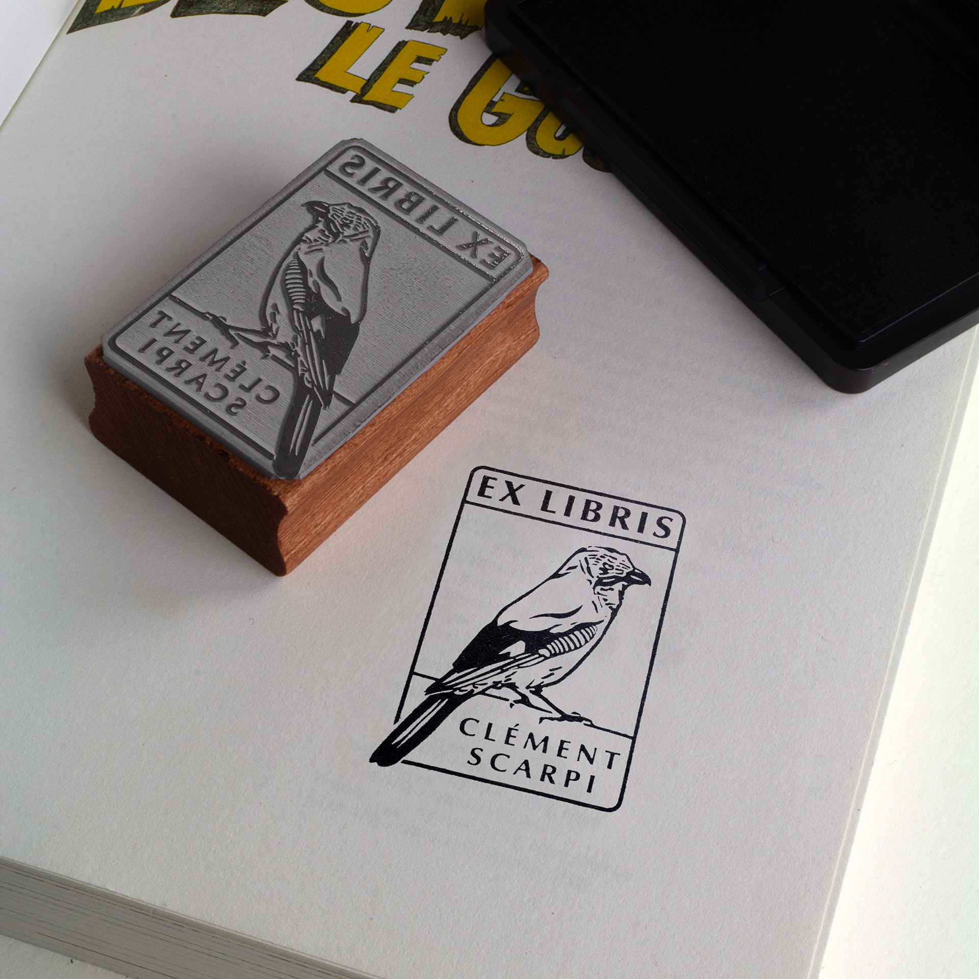 A wooden stamp with a bird illustration and the text EX LIBRIS CLÉMENT SCARPI sits on a book near a black ink pad—perfect inspiration for your Adobe Portfolio or personalized website. The stamp’s design is printed below it on the book’s page.