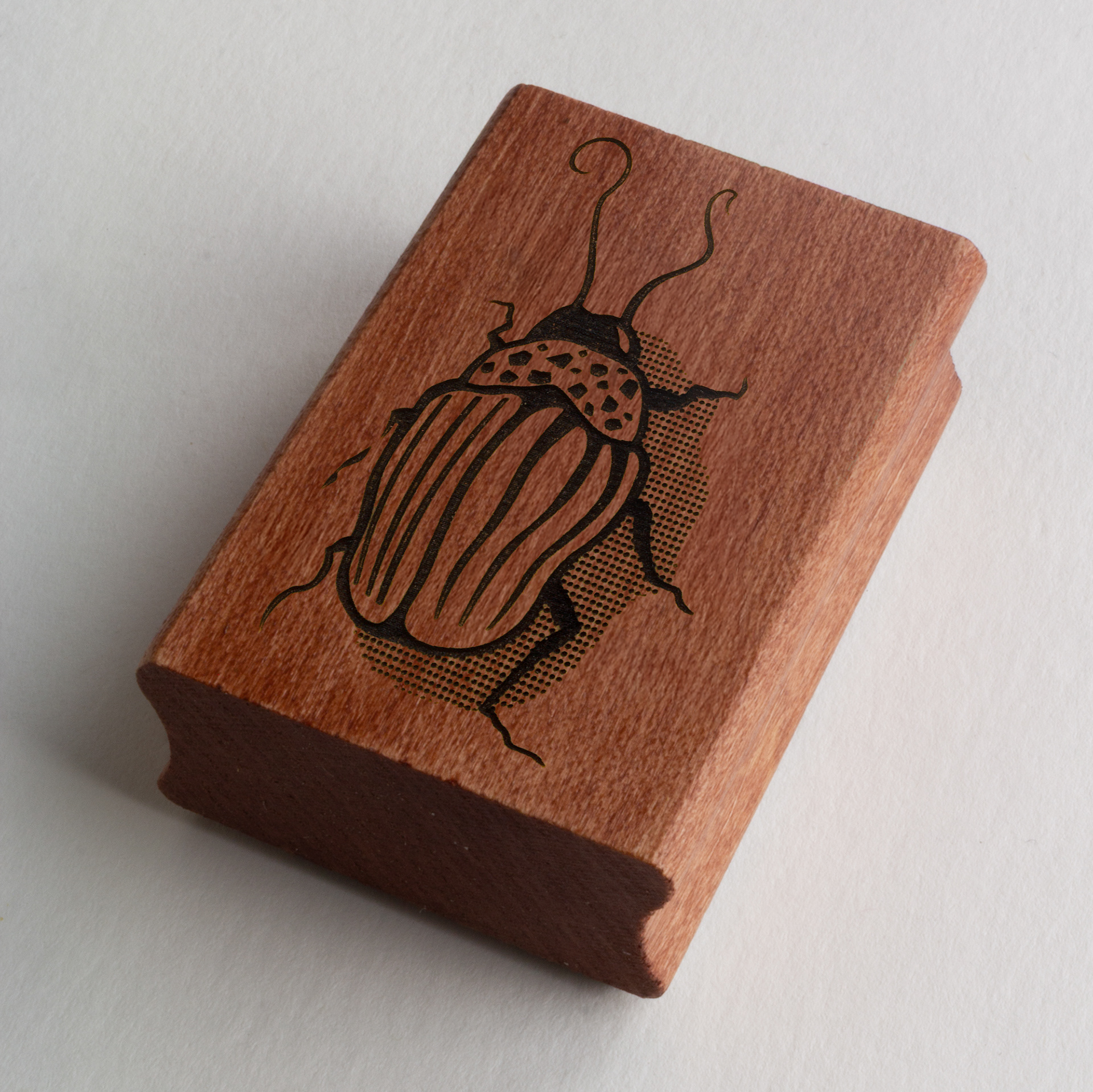 A rubber stamp with a insect illustration and the text “EX LIBRIS CLÉMENT SCARPI” lies next to its stamped impression on white paper.