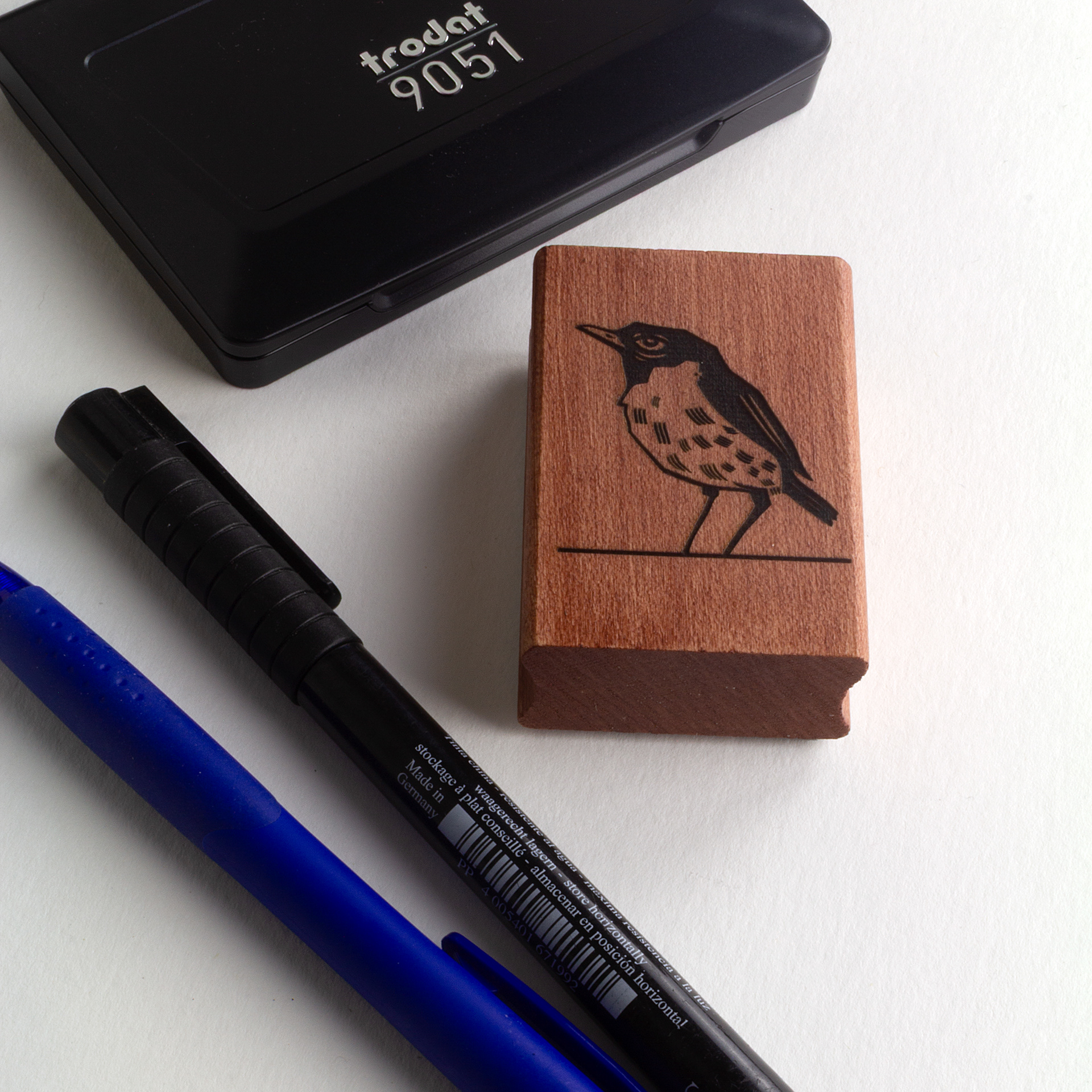 A rubber stamp with a bird illustration and the text “EX LIBRIS CLÉMENT SCARPI” lies next to its stamped impression on white paper.