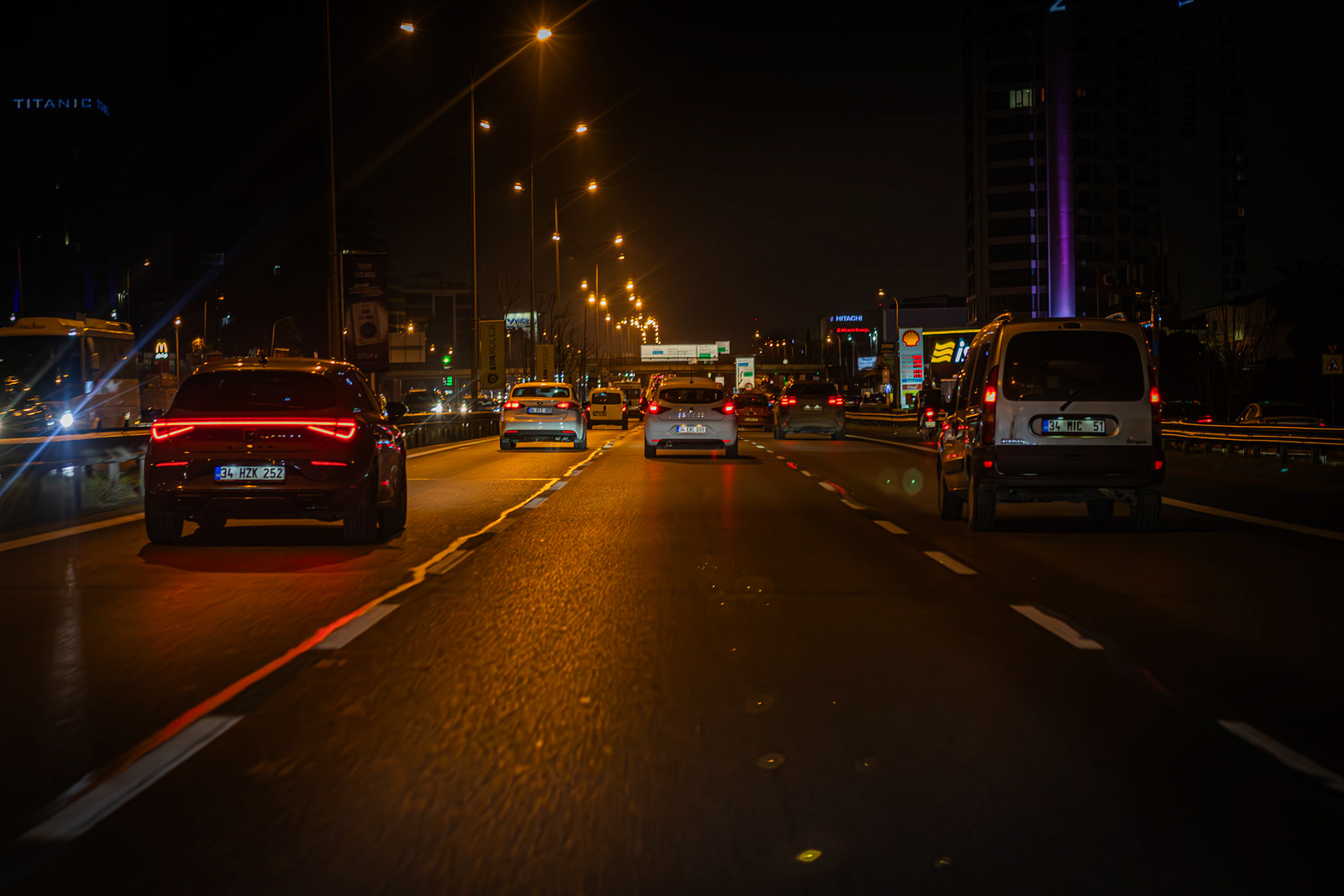 E-5'te gece geç saatlerde, İstanbul'un trafiği hala akıyor. Arabaların farları, karanlığı aydınlatırken, gölgeli siluetler şehrin uyumadığını fısıldıyor. Bu manzara, şehrin canlılığını ve dinamizmini yansıtıyor. Aynı zamanda, trafikte mahsur kalan insanların sabırsızlığını ve yorgunluğunu da hissettiriyor.