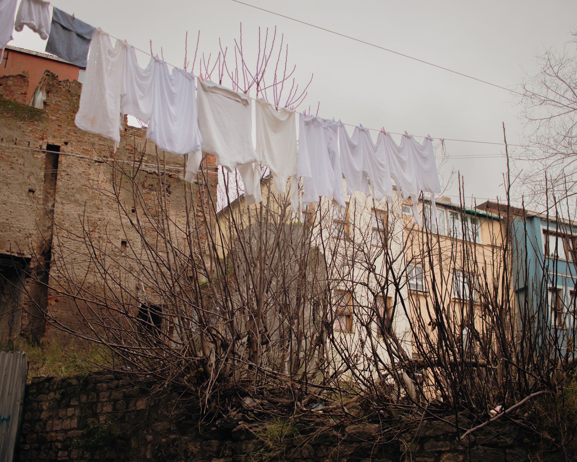 Balat'ın tarihi ve renkli evleri arasında, bir evin karşısındaki tarihi taş duvara ip çekilmiş ve bembeyaz çamaşıırlar kurumaya asılmış. Bu manzara, geleneksel yaşamın ve sadeliğin güzel bir örneğini sunuyor. Beyaz çamaşıırlar, eski taş duvarla kontrast oluşturarak göze hoş gelen bir görüntü oluşturuyor.