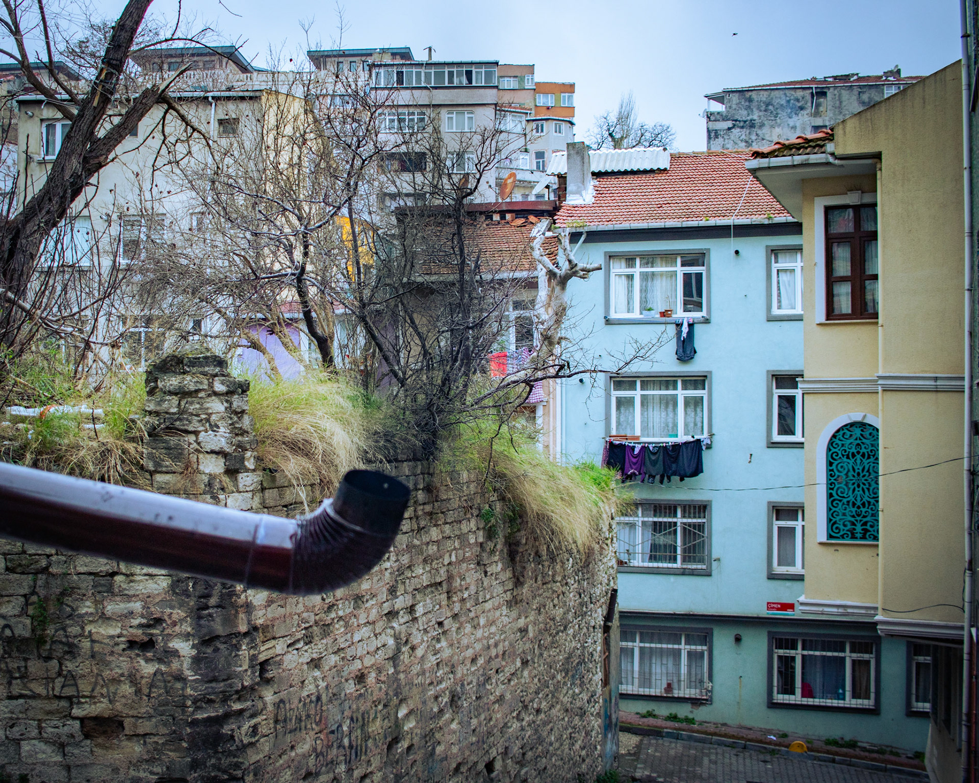 Balat'ın tarihi ve renkli evleri arasında, bir evin bacasından yükselen duman, kış mevsiminin sıcak bir tablosunu çiziyor. Duman, gri gökyüzüne doğru uzanırken, etrafındaki renkli evlerle kontrast oluşturuyor. Bu manzara, geçmişe özlem uyandıran nostaljik bir atmosfere sahip.