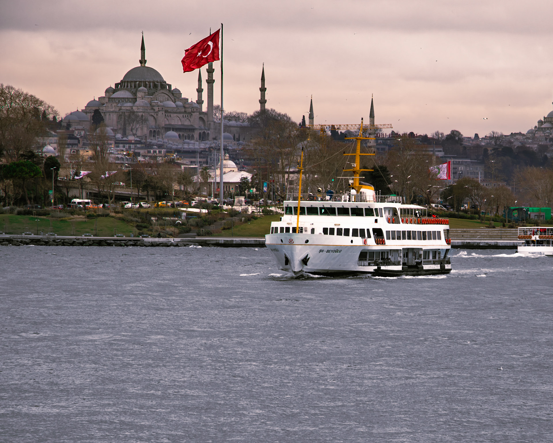 Tarihi Yarımada'dan ayrılan ŞH-Beyoğlu vapuru, Sultanahmet Camii ve Şanlı Türk Bayrağı'nın heybetli manzarasının önünden geçiyor. Bu kare, adeta bir tabloyu andırıyor. Bir yanda tarihi caminin ihtişamı, diğer yanda gururla dalgalanan bayrağımız, vatan sevgisini ve tarihi bilinci körüklüyor. Vapurun denizin üzerinde bıraktığı izler ise adeta bir veda mesajı gibi, geride kalan tarihi yarımadaya selam veriyor.