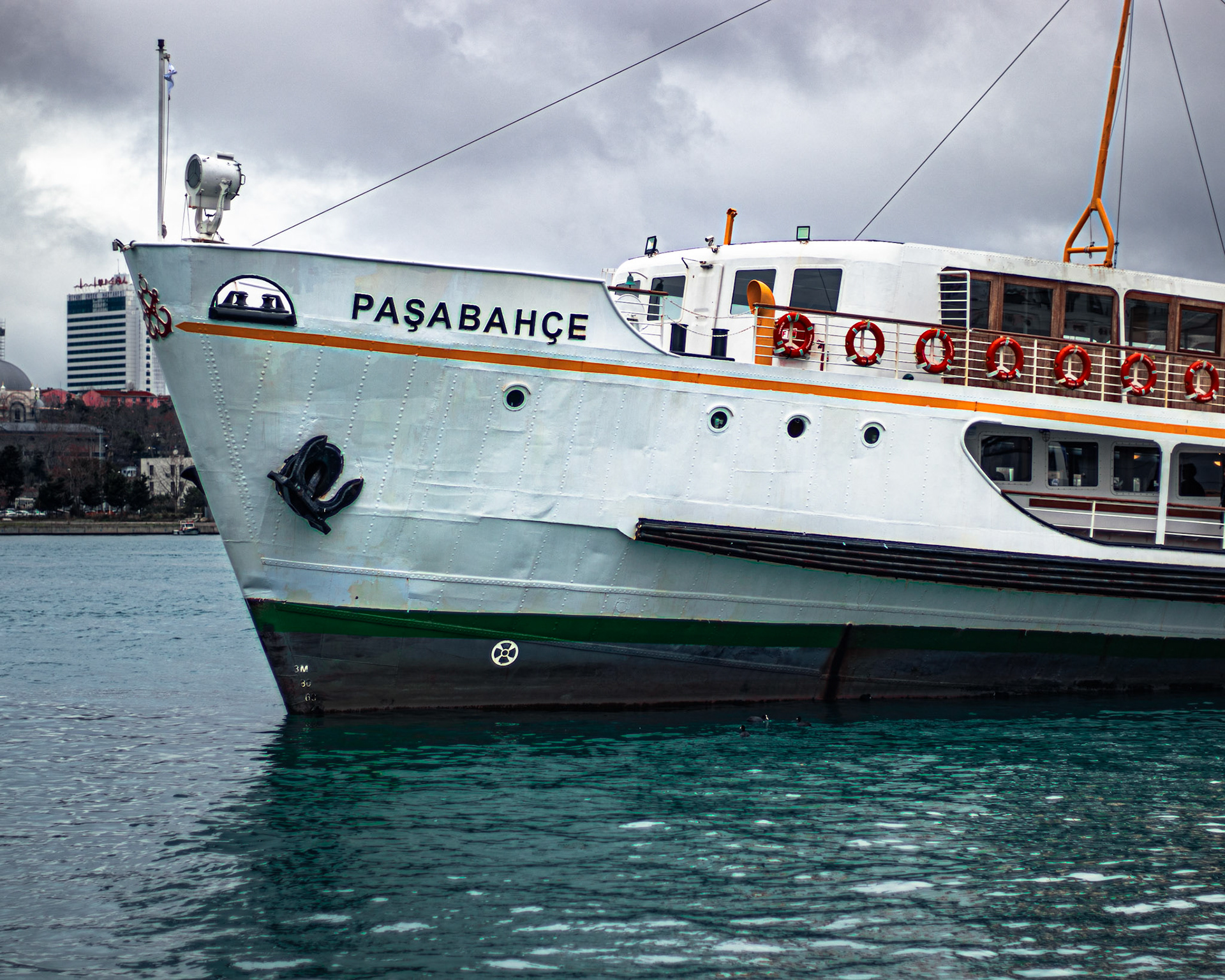 Kadıköy İskelesi'nin canlı atmosferinin tam ortasında, Paşabahçe vapuru sessizce bekliyor. Yolcuların telaşı ve martıların sesleri arasında, vapur adeta bir meditasyona dalmış gibi huzurlu bir duruş sergiliyor. Bu durgunluk, şehrin karmaşasından bir kaçış noktası sunuyor ve izleyene huzur veriyor. Vapurun gövdesine yansıyan güneş ışıkları ve denizin dalgaları, bu manzaraya ayrı bir güzellik katıyor.