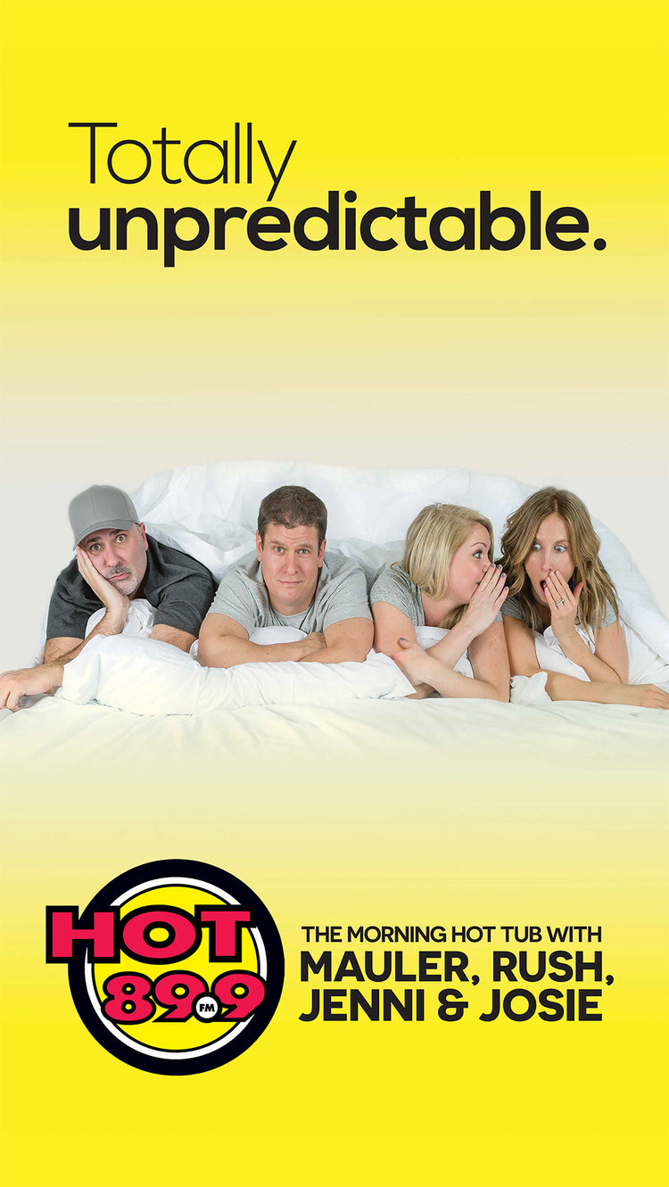 Hot 89.9 Banner. Photo is the morning show hosts sharing a bed. The text reads above their heads "Totally unpredictable."