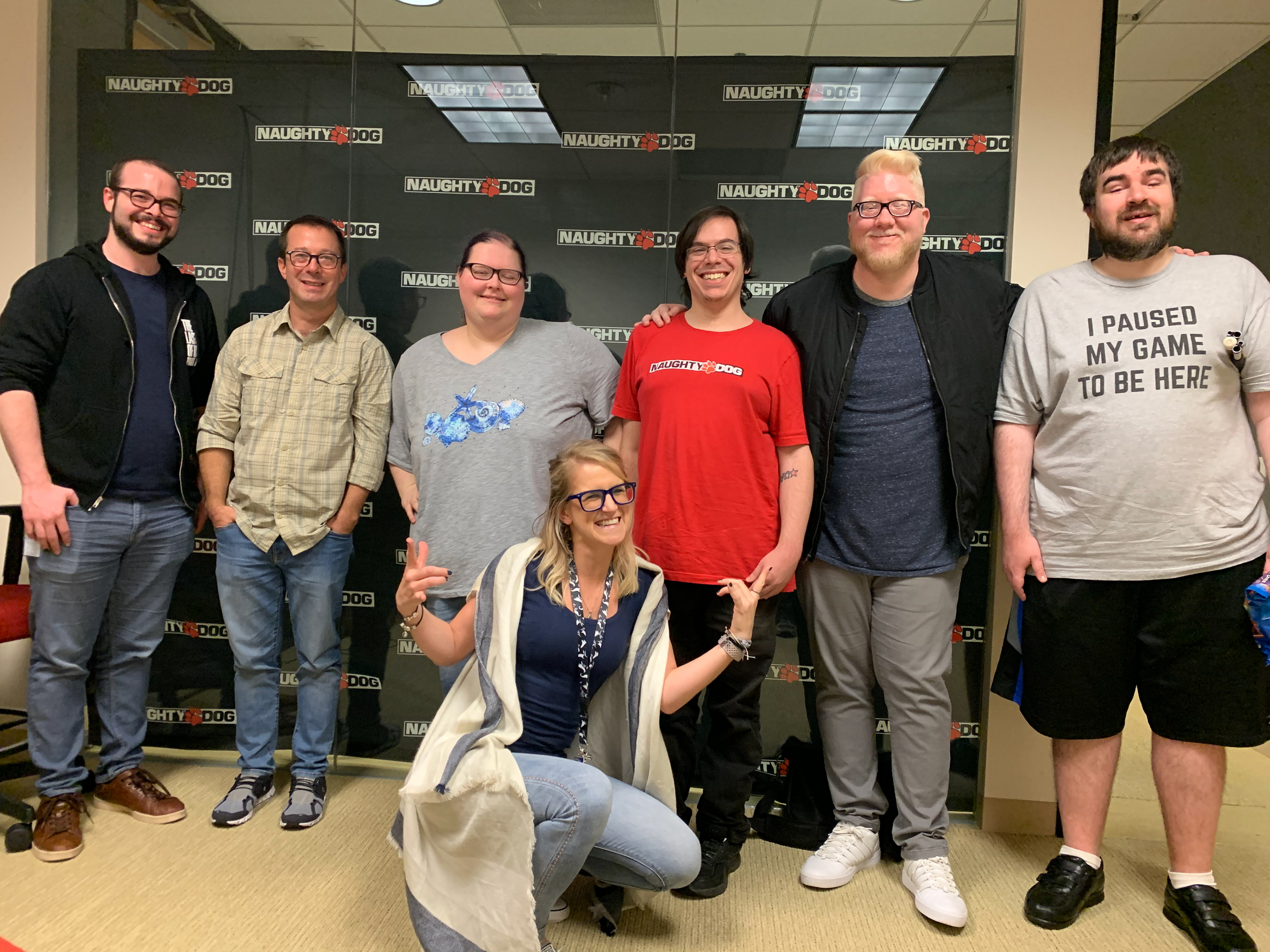 Myself and several QA Developers from Sony and Naughty Dog in a group photo in front of a Naughty Dog wall banner.